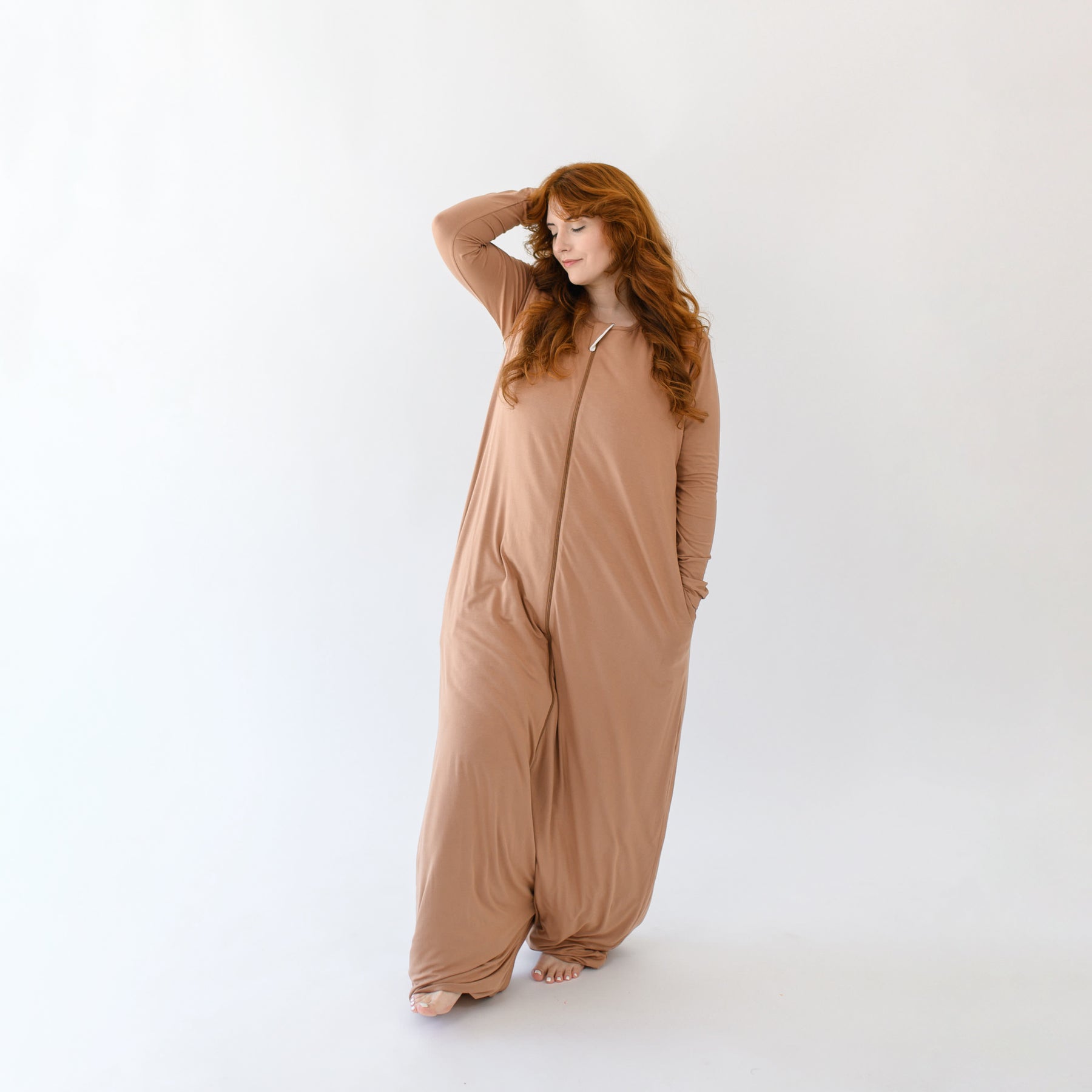 Model standing with one hand in her hair and the other hand in the pocket of the Adult Sleep Bag Walker in Latte