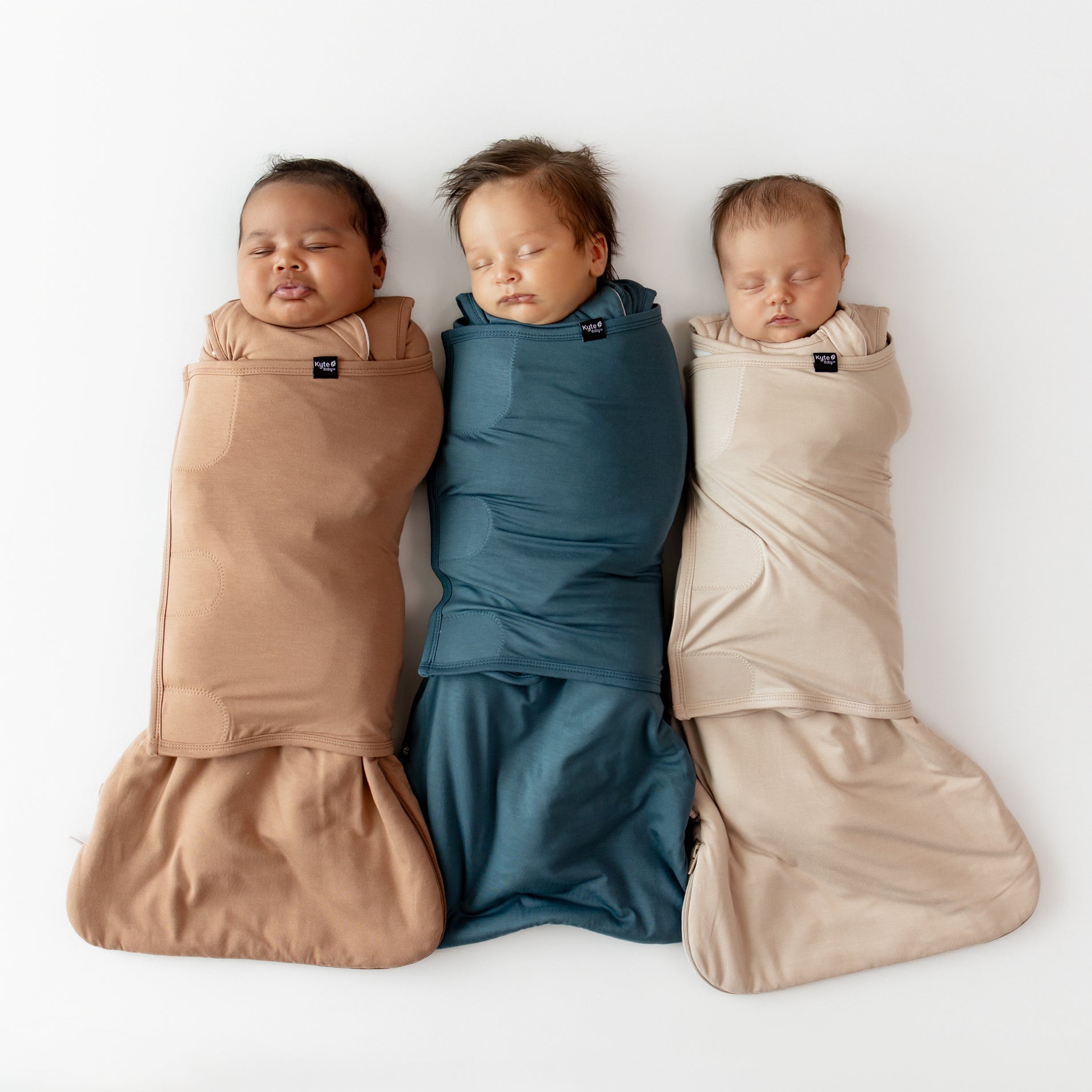 Three sleeping babies laying side by side wearing the sleep bag swaddlers from the fall collection