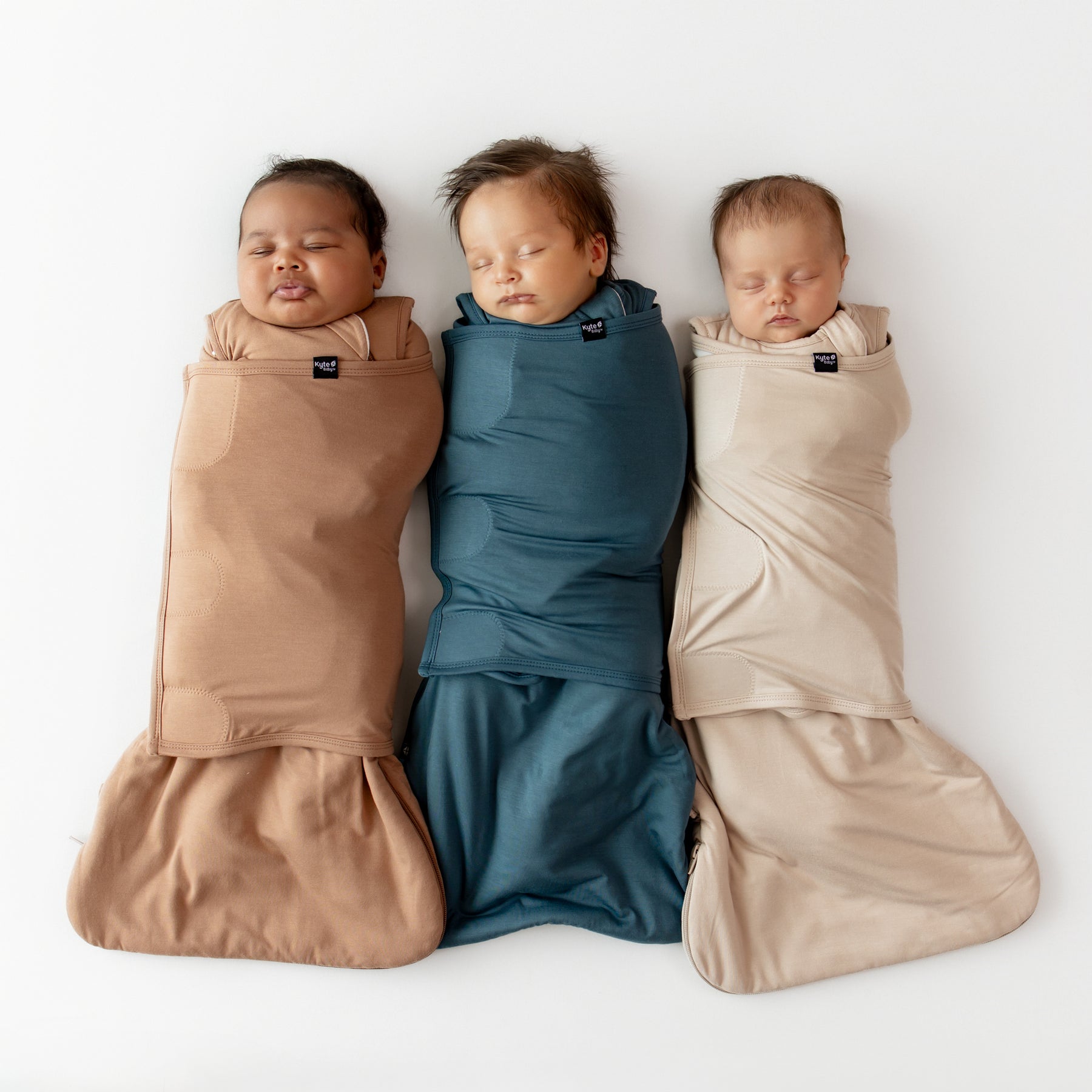 Three sleeping babies laying side by side wearing the sleep bag swaddlers from the fall collection