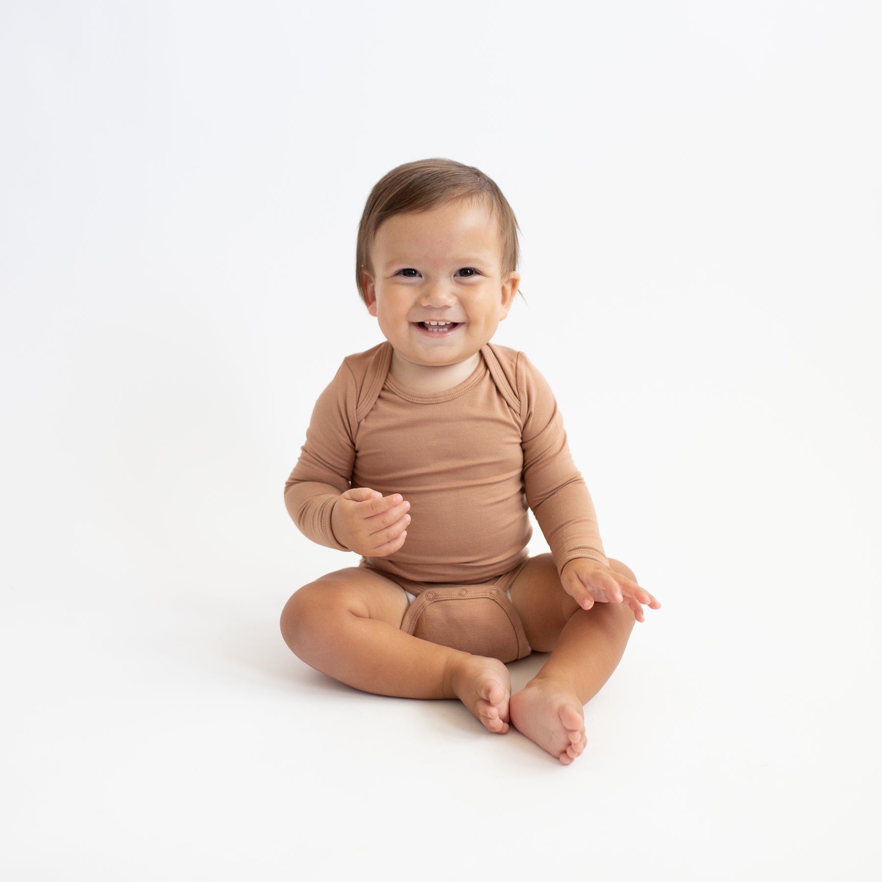 Smiling toddler sitting on the floor wearing the Long Sleeve Bodysuit in Latte