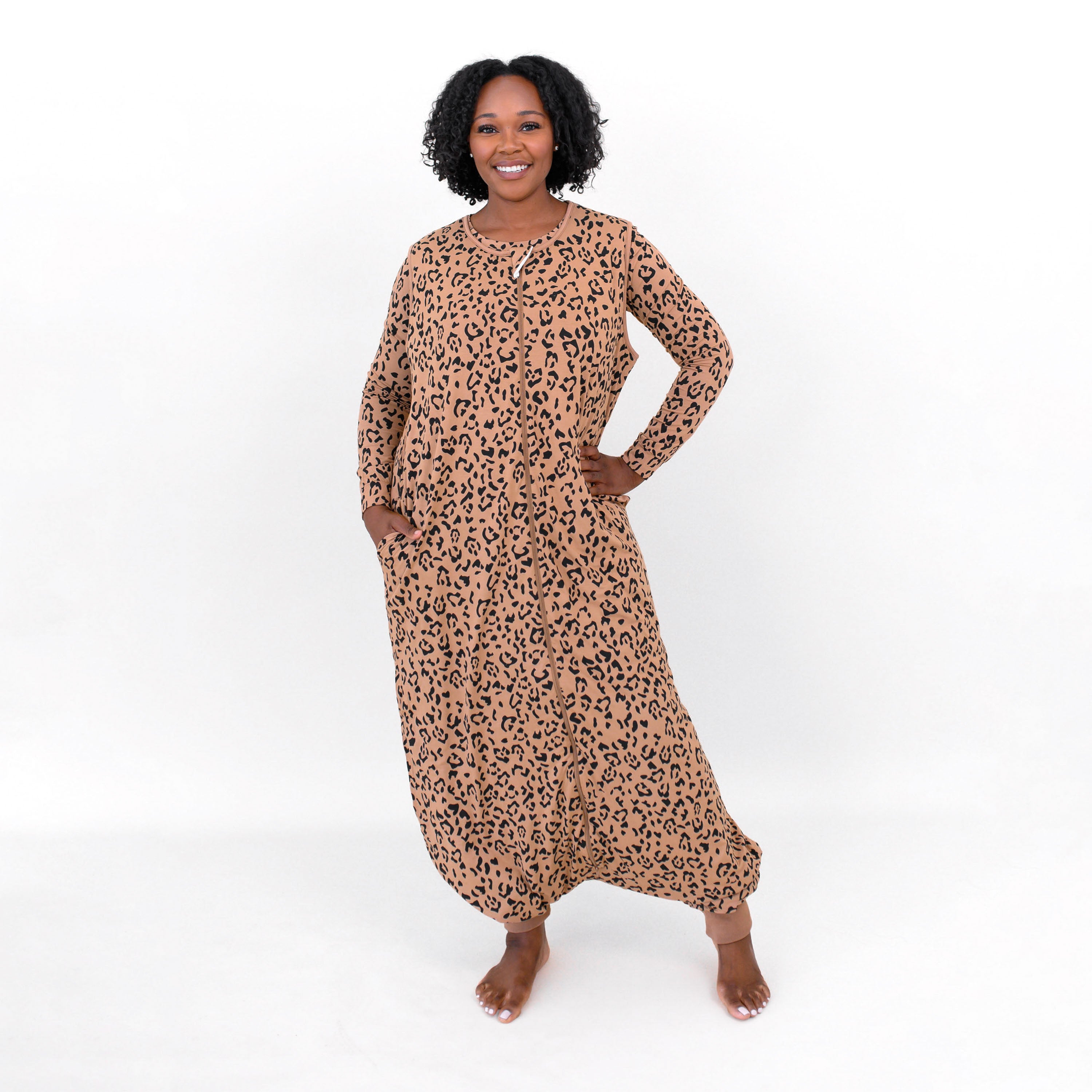 Female model standing with one hand on hip and the other hand in the pocket of the Adult Sleep Bag Walker in Latte Leopard in front of a white backdrop