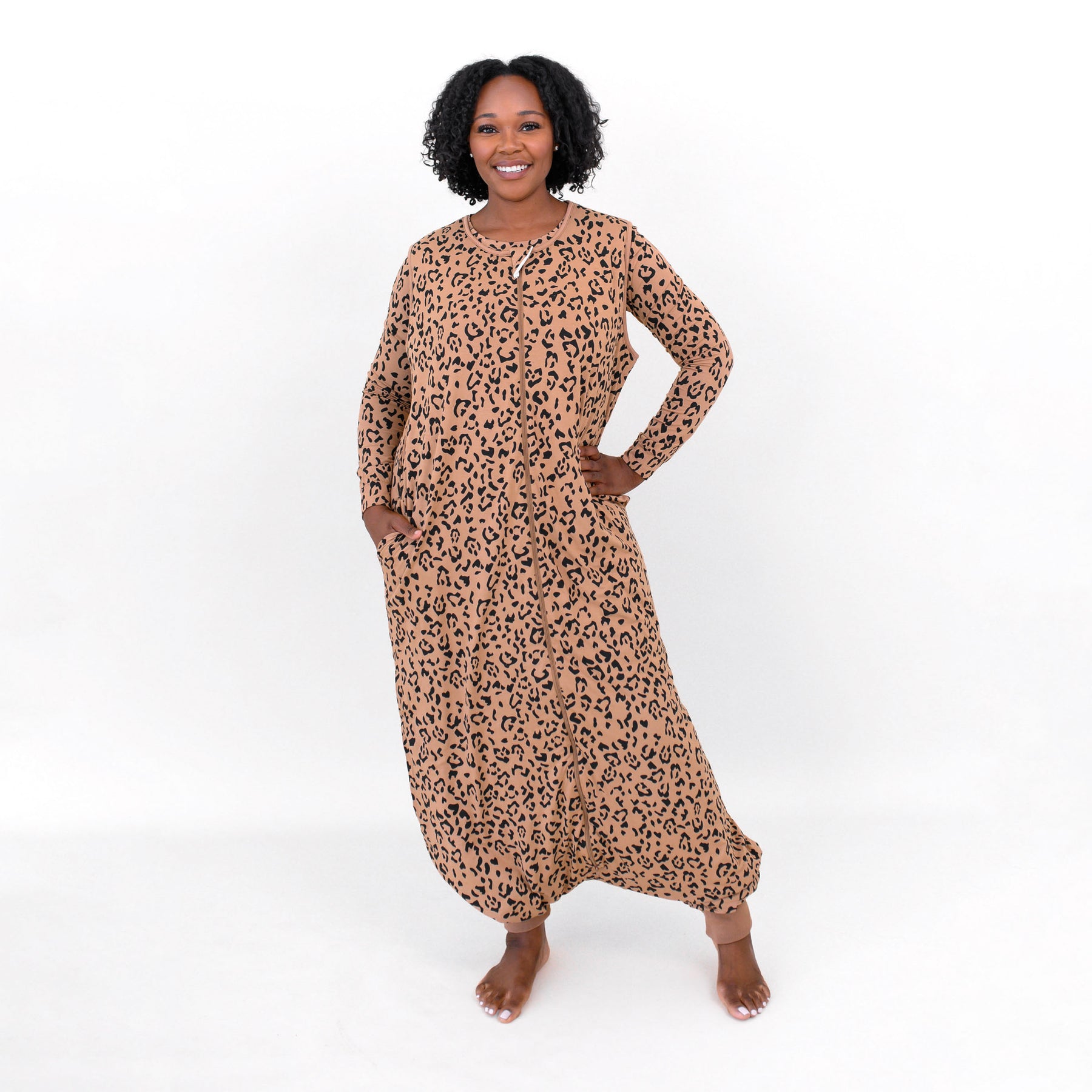 Female model standing with one hand on hip and the other hand in the pocket of the Adult Sleep Bag Walker in Latte Leopard in front of a white backdrop