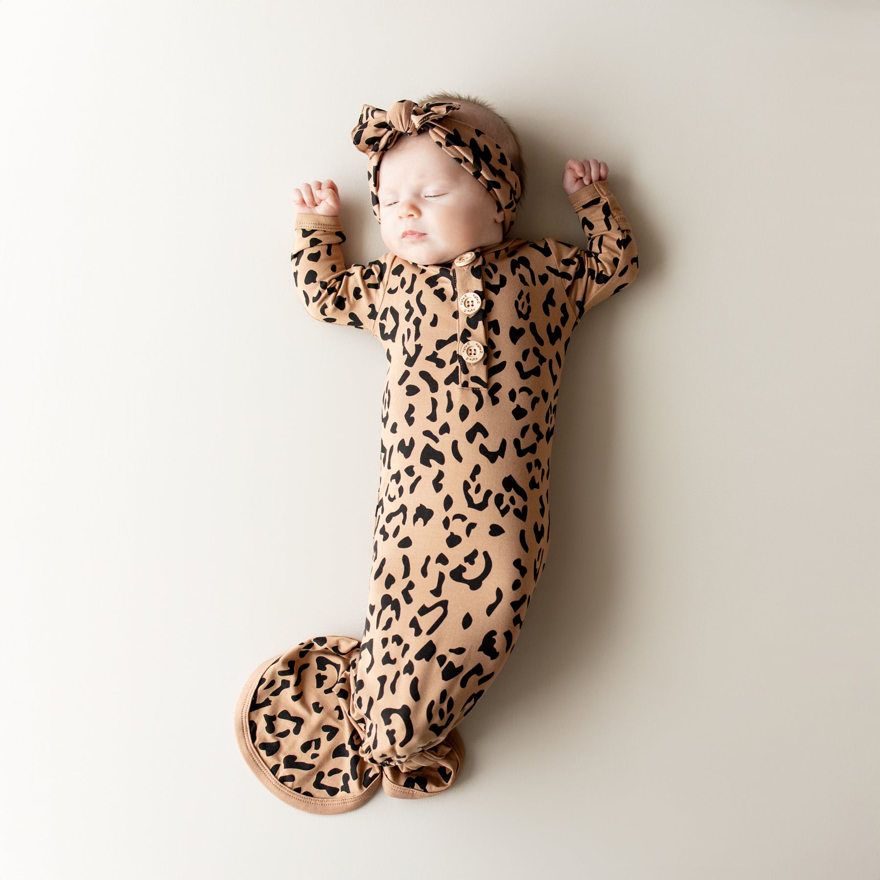 Sleeping infant wearing the Knotted Gown with Bow Set in Latte Leopard with her hands up by her head