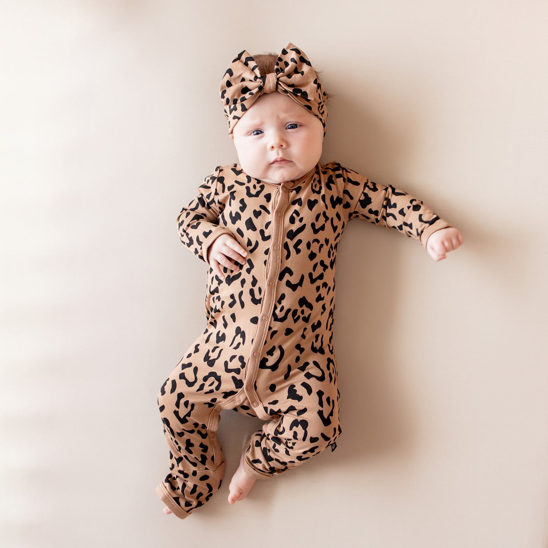 Baby wearing snap romper pajamas and matching bow headband in Latte Leopard