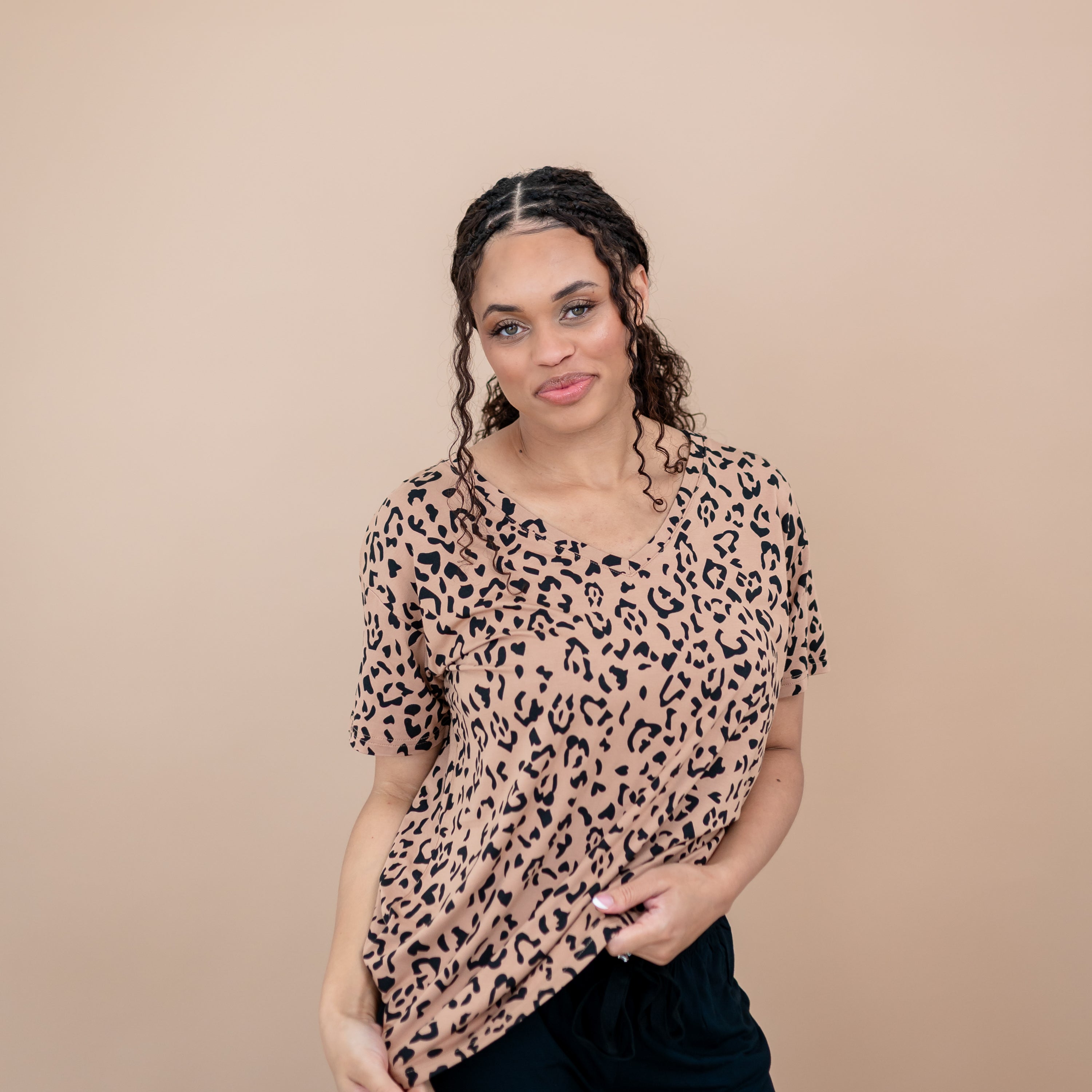 Smiling model wearing the Women's Relaxed Fit V-Neck in Latte Leopard and black pants standing in front of a taupe background