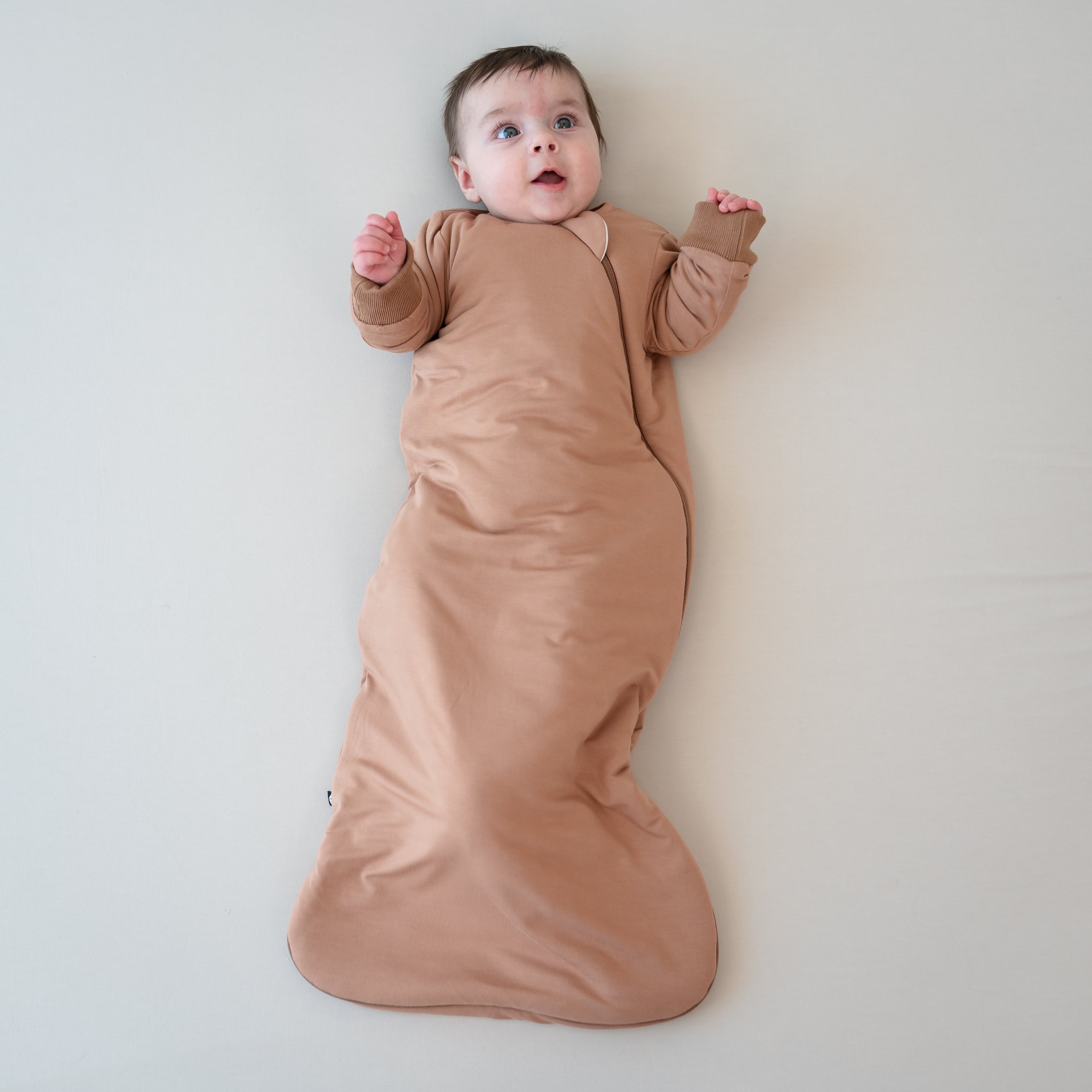 Infant laying down wearing the Slumber Bag in Latte