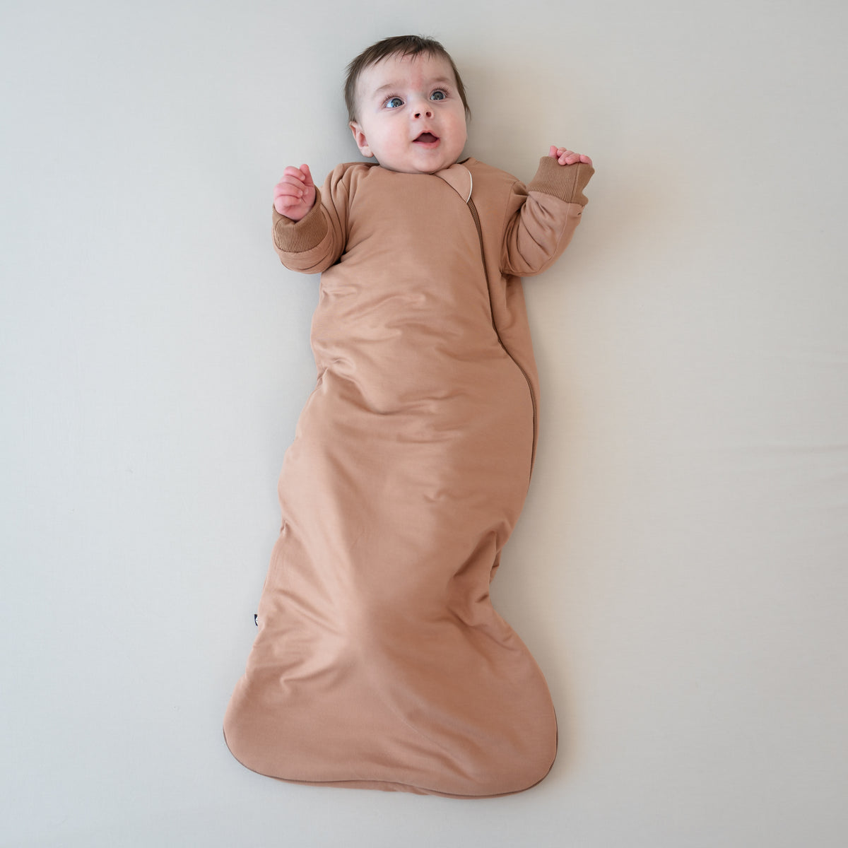 Infant laying down wearing the Slumber Bag in Latte