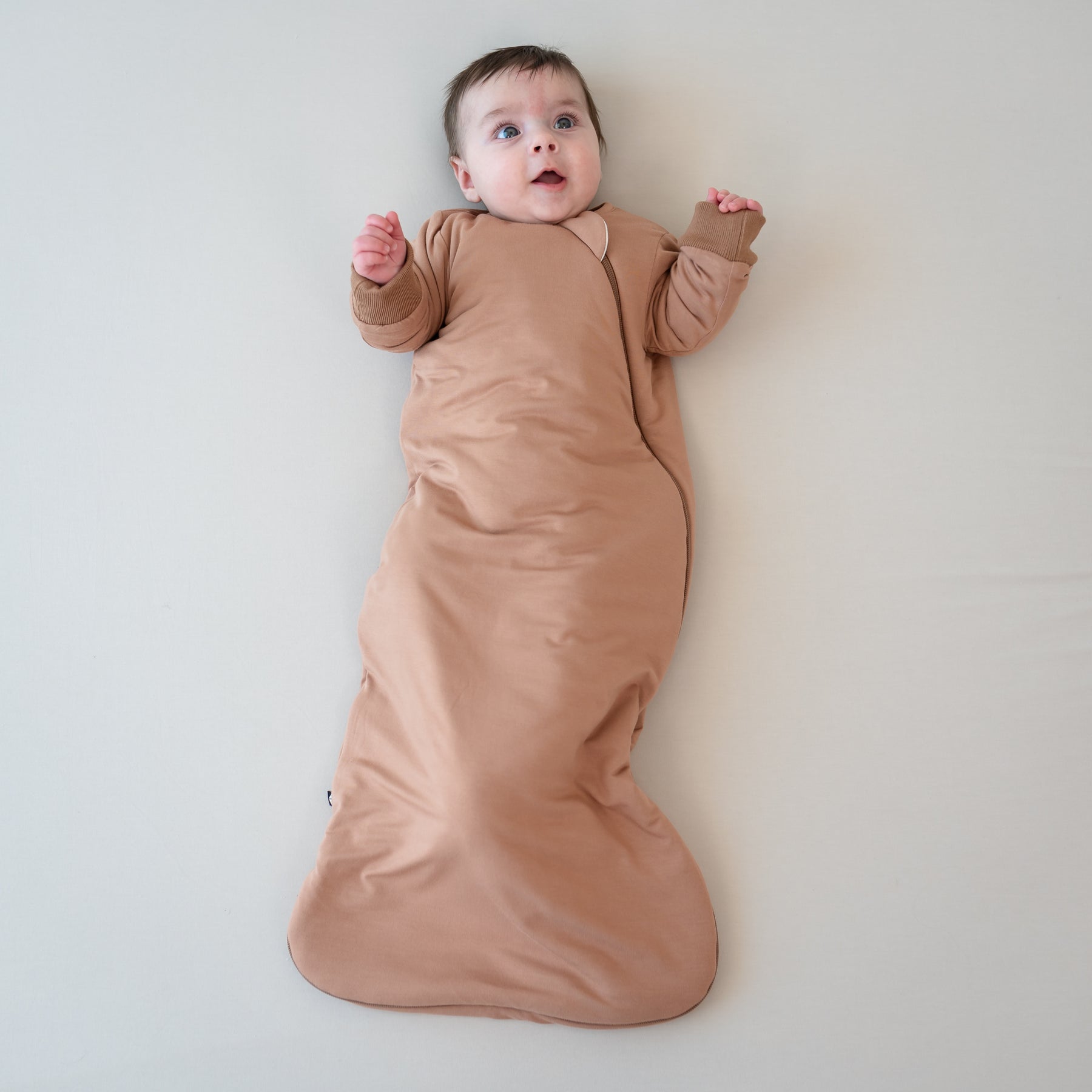 Infant laying down wearing the Slumber Bag in Latte