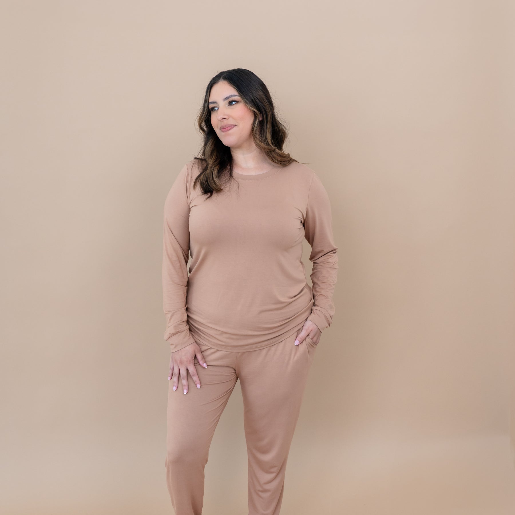 Smiling female model standing with one hand in the pocket of the Women's Jogger Pajama Set in Latte pants looking off to the side