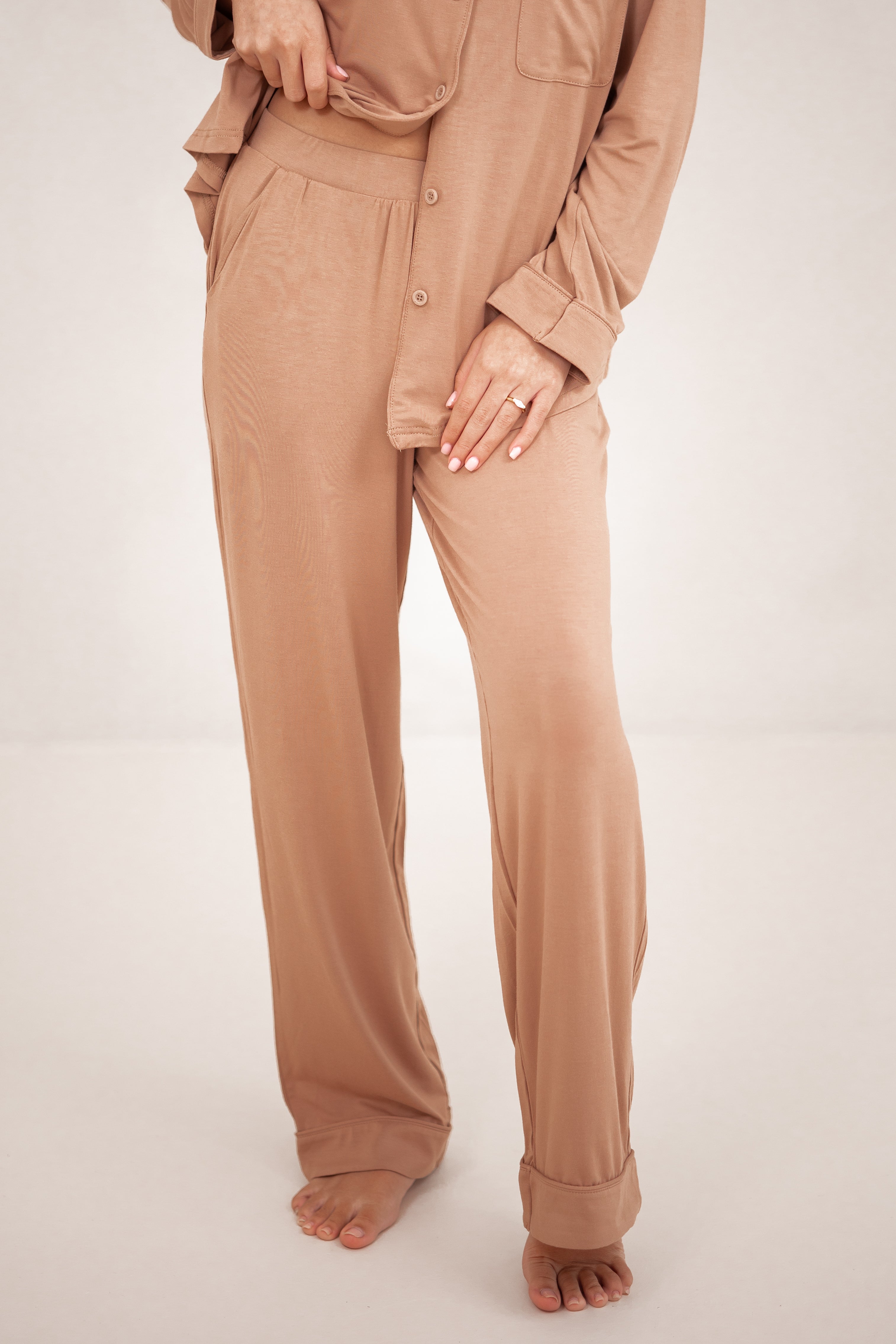 A model wearing the Long-Sleeved Women's Pajama Set in Latte with Latte Trim with emphasis on the pants with the bottom hem of the shirt pulled up