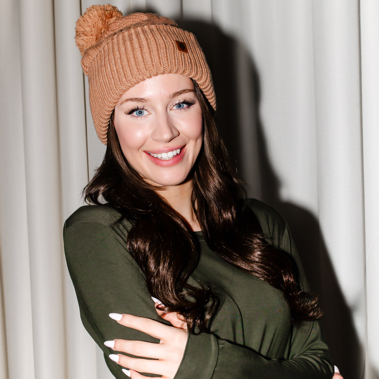 Smiling female modeling the Cable Knit Adult Pom Beanie in Latte