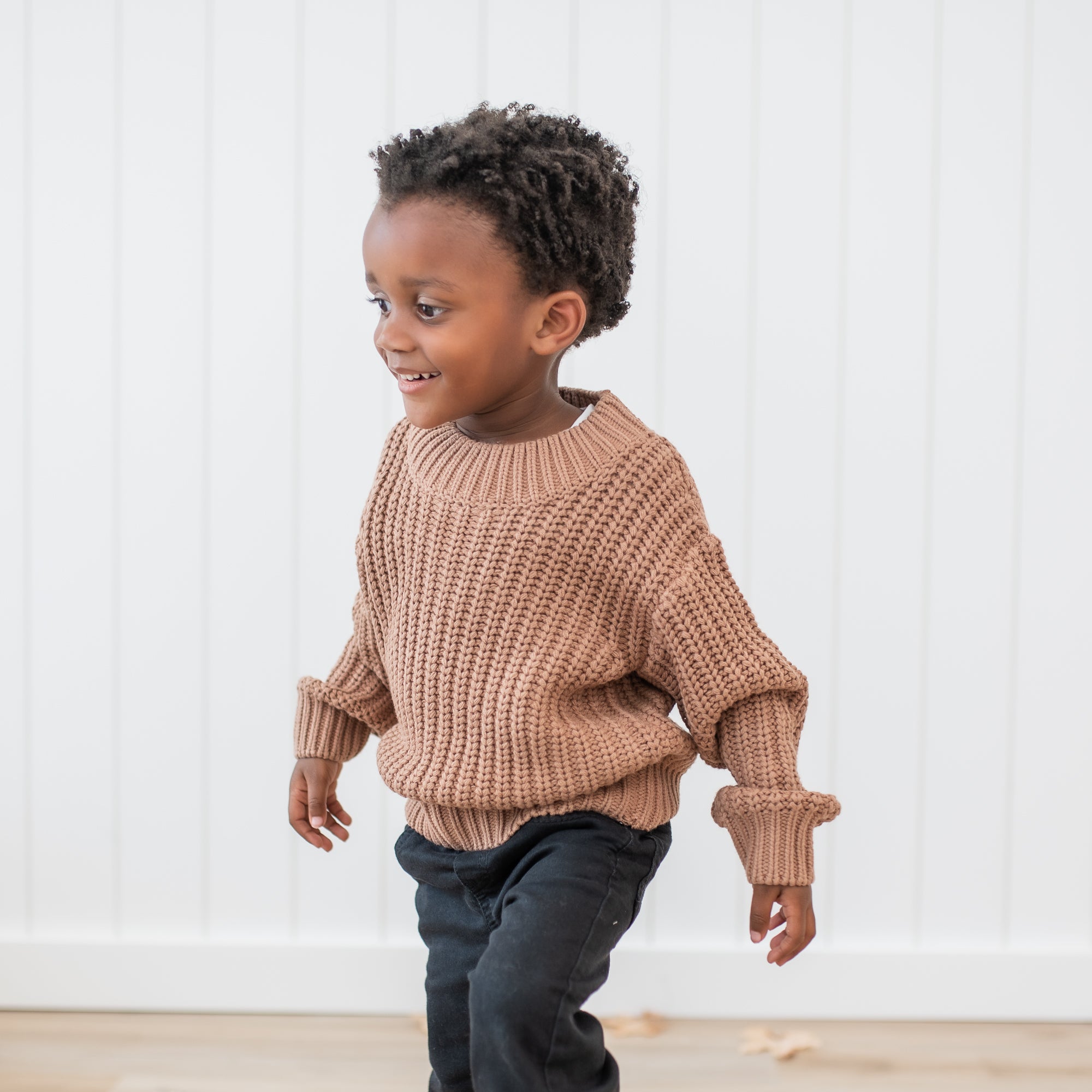 Close up of young boy wearing the Chunky Knit Sweater in Latte and black jeans