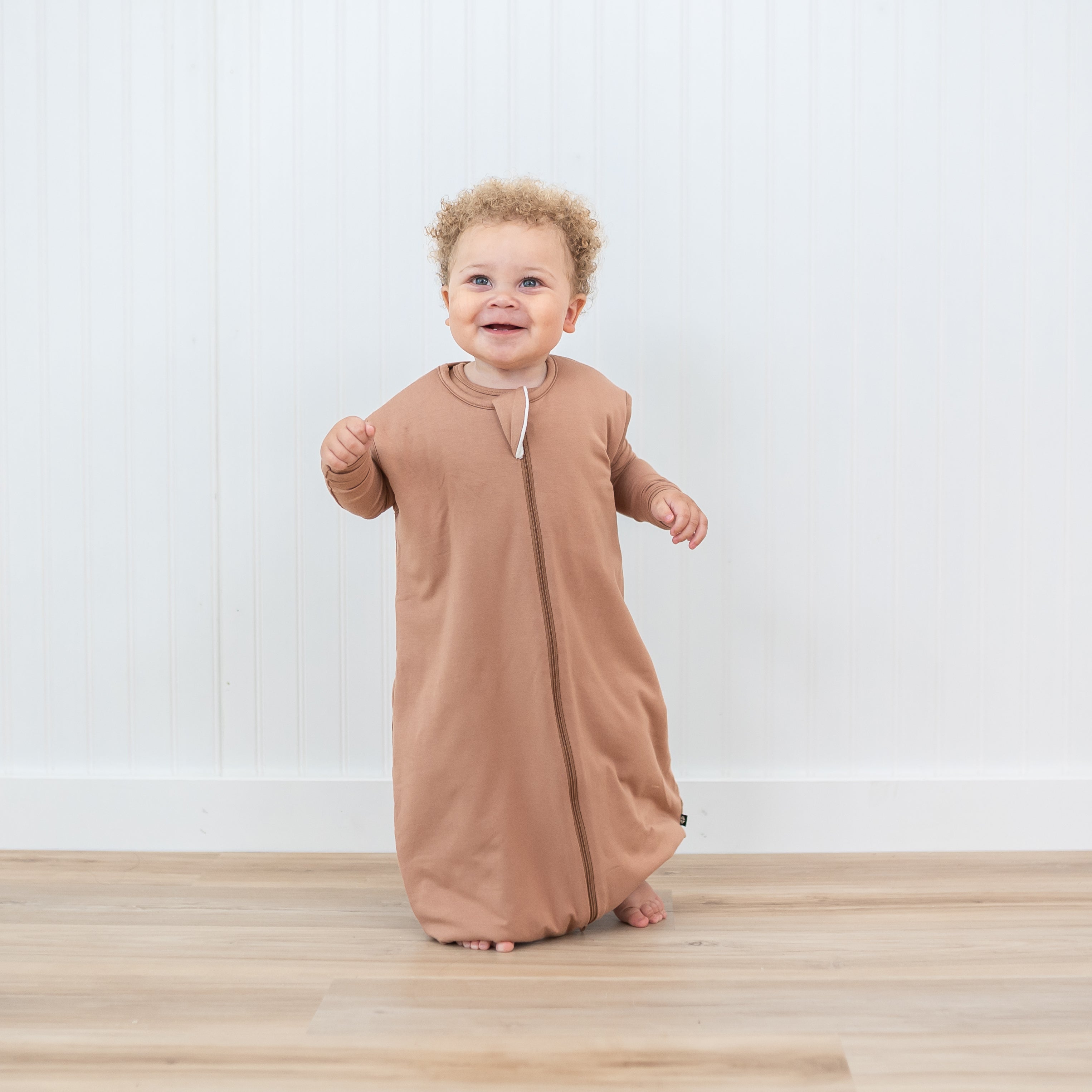 Toddler walking in the Sleep Bag Walker in Latte 1.0 with matching long sleeve toddler pajamas on underneath