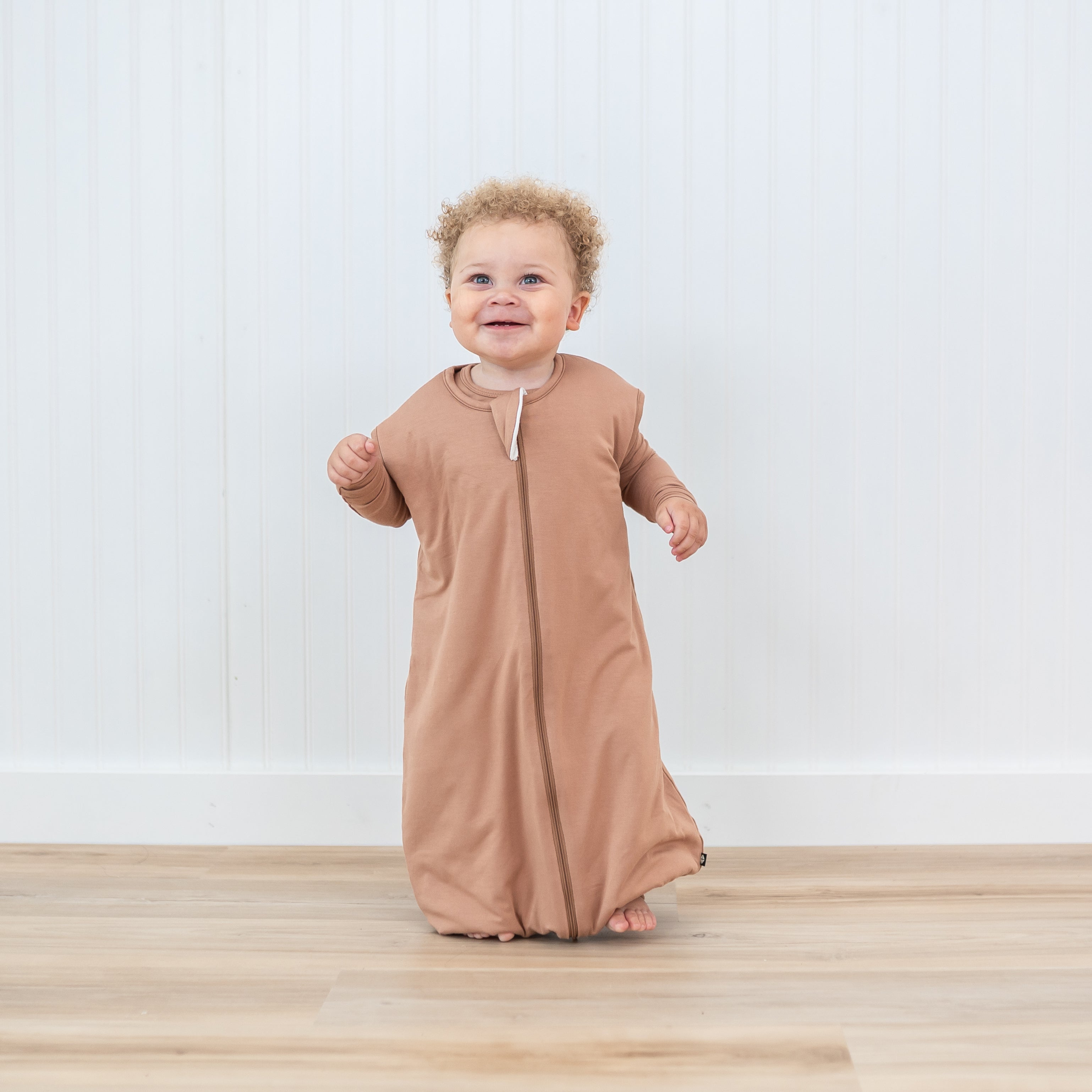 Toddler walking in the Sleep Bag Walker in Latte 1.0 with matching long sleeve pajamas underneath