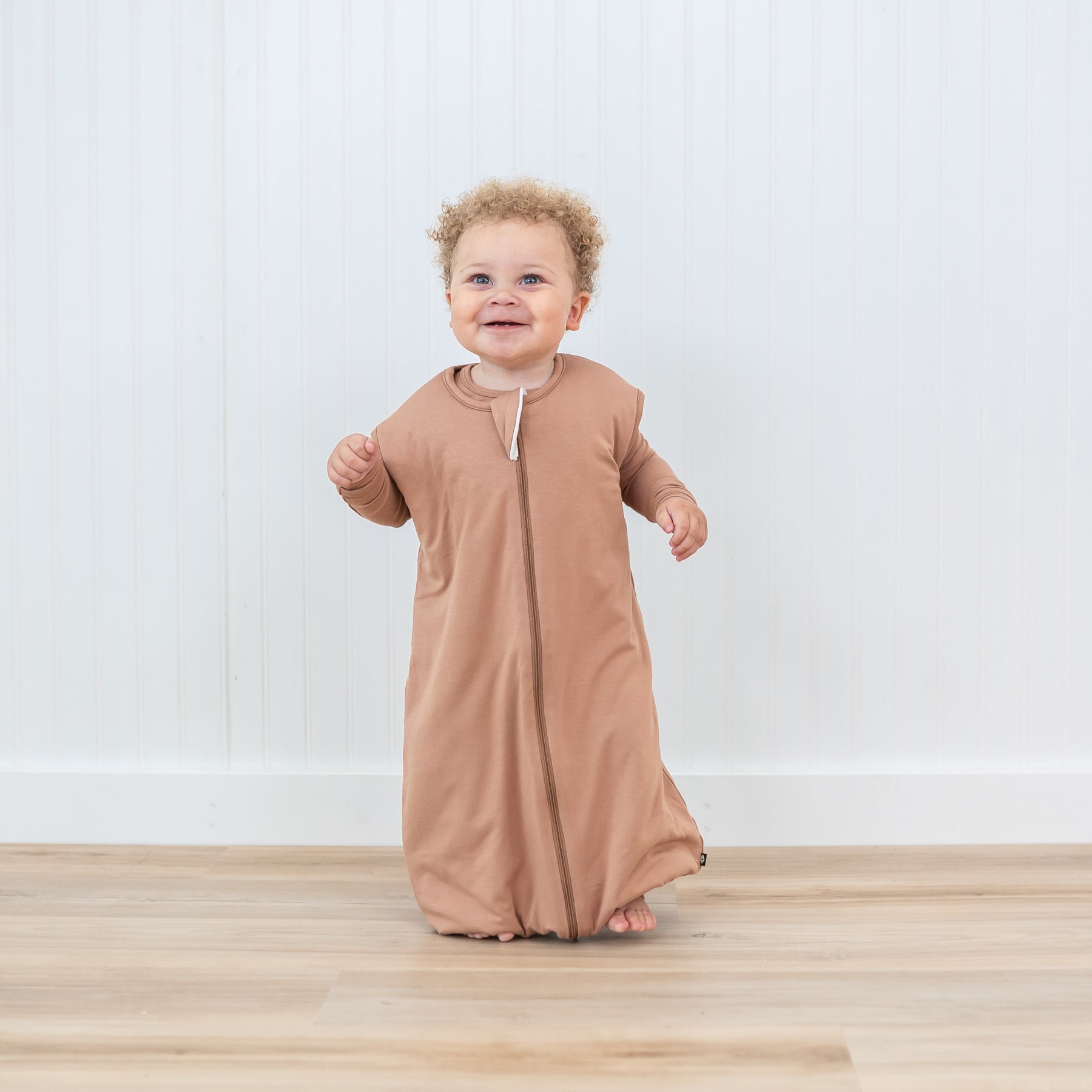Toddler walking in the Sleep Bag Walker in Latte 1.0 with matching long sleeve pajamas underneath