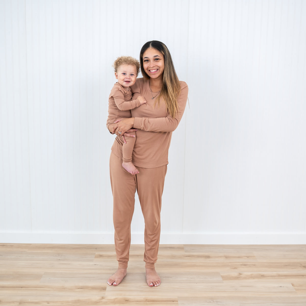 Smiling mother wearing the Women's Jogger Pajama Set in Latte holding child wearing matching long sleeve toddler pajamas