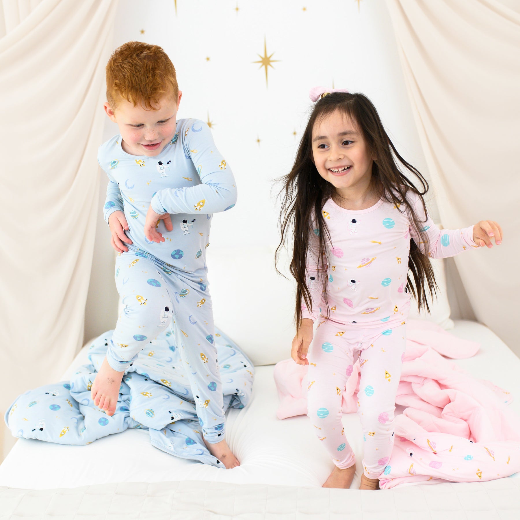 toddlers jumping on bed wearing ice and sakura space pajamas with matching blankets on bed