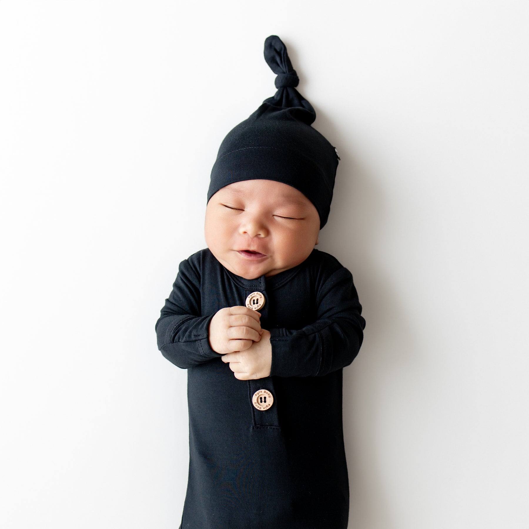 Baby wearing a black outfit and hat against a white background