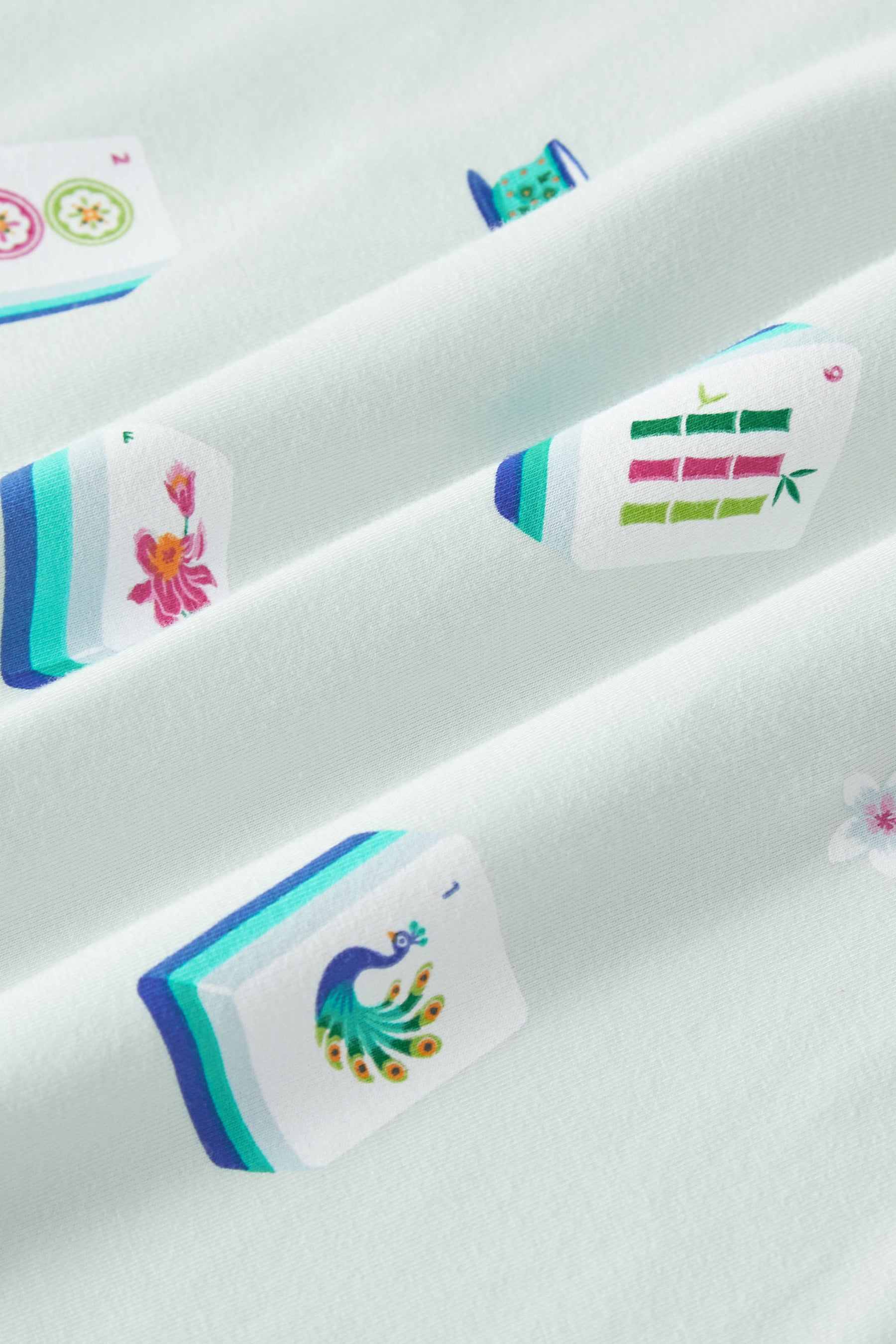 An all-over print featuring: white Mahjong tiles with a navy and turquoise back and various artworks; white jasmine flowers with pink centers and green leaves; white dice with pink, turquoise, and green markings; and turquoise teacups with navy trim, over a pale turquoise background color named Dew.