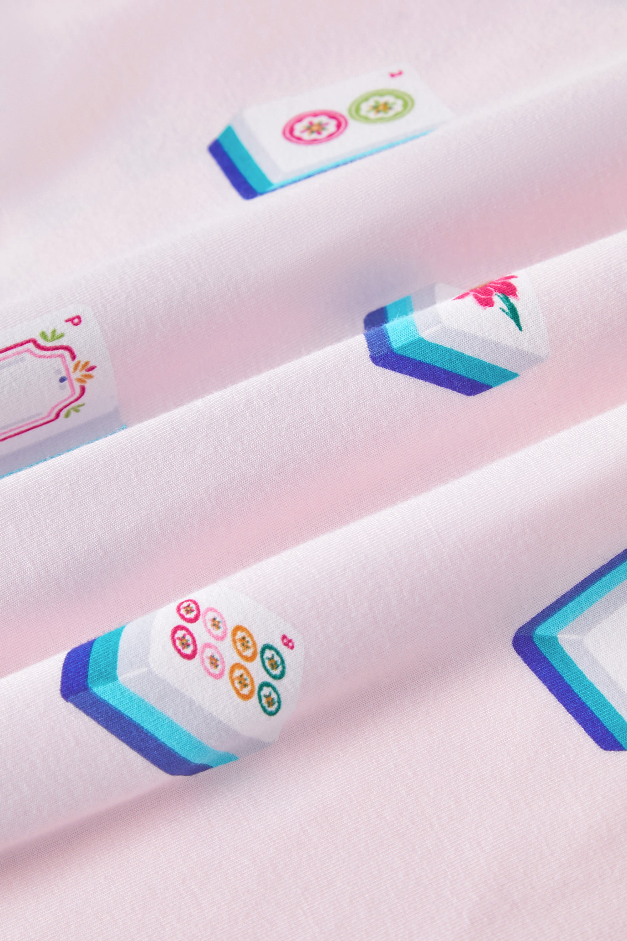 An all-over print featuring: white Mahjong tiles with a navy and turquoise back and various artworks; white jasmine flowers with pink centers and green leaves; white dice with pink, turquoise, and green markings; and pink teacups with navy trim, over a pale pink background color named Sakura.