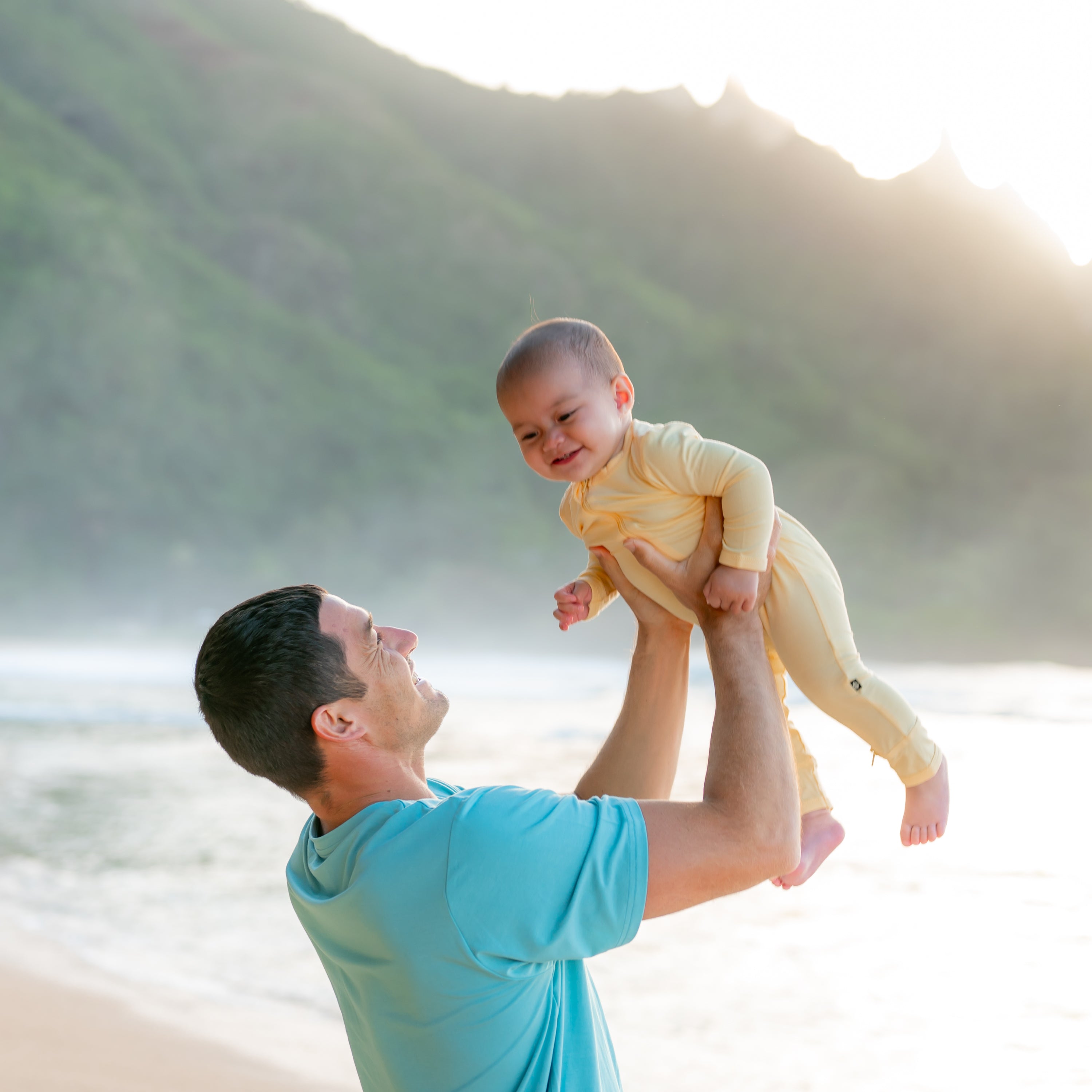 Dad wearing Men's Crew Neck Tee in Makai holding up baby in Lilikoi romper