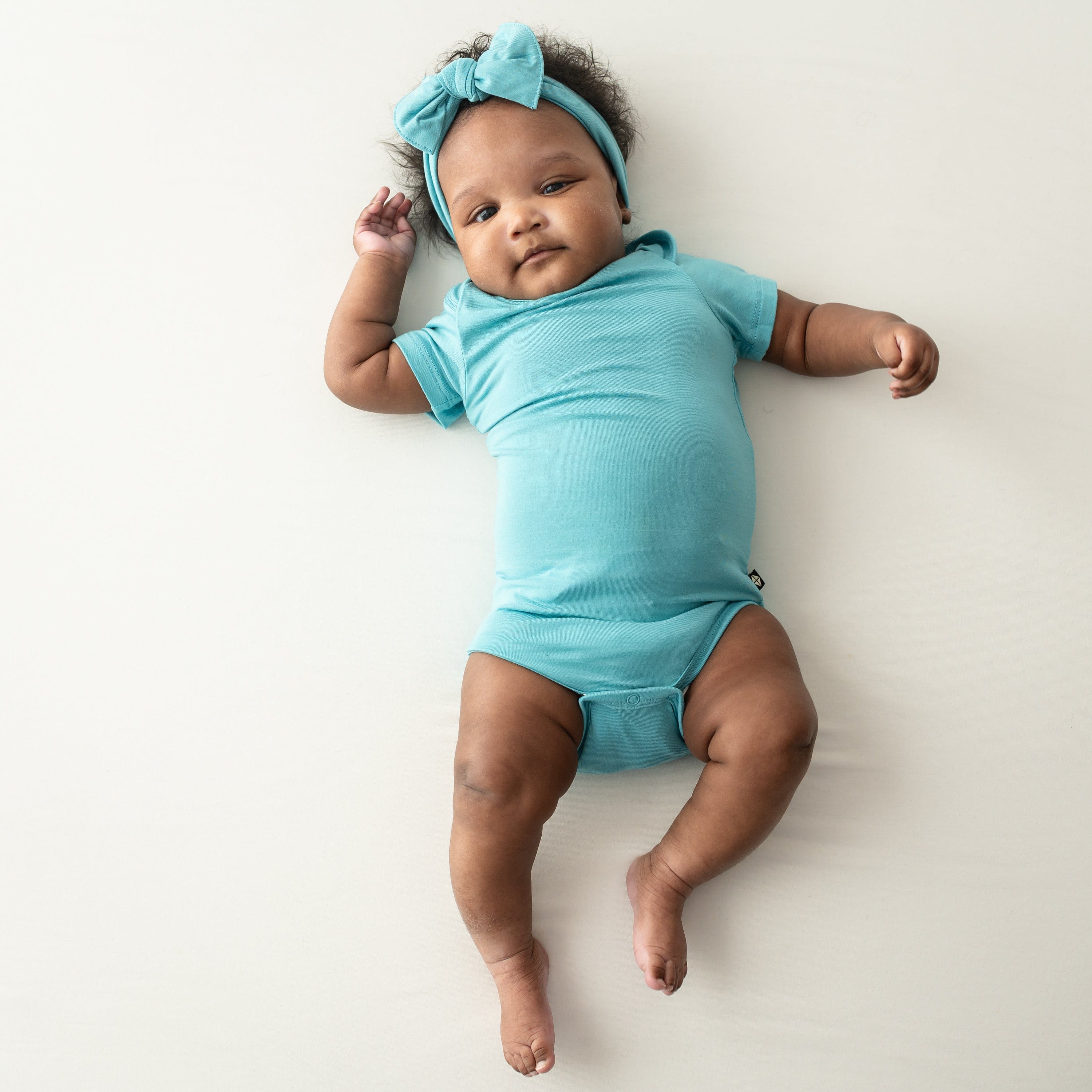 short sleeve bodysuit and bow in makai on a baby model