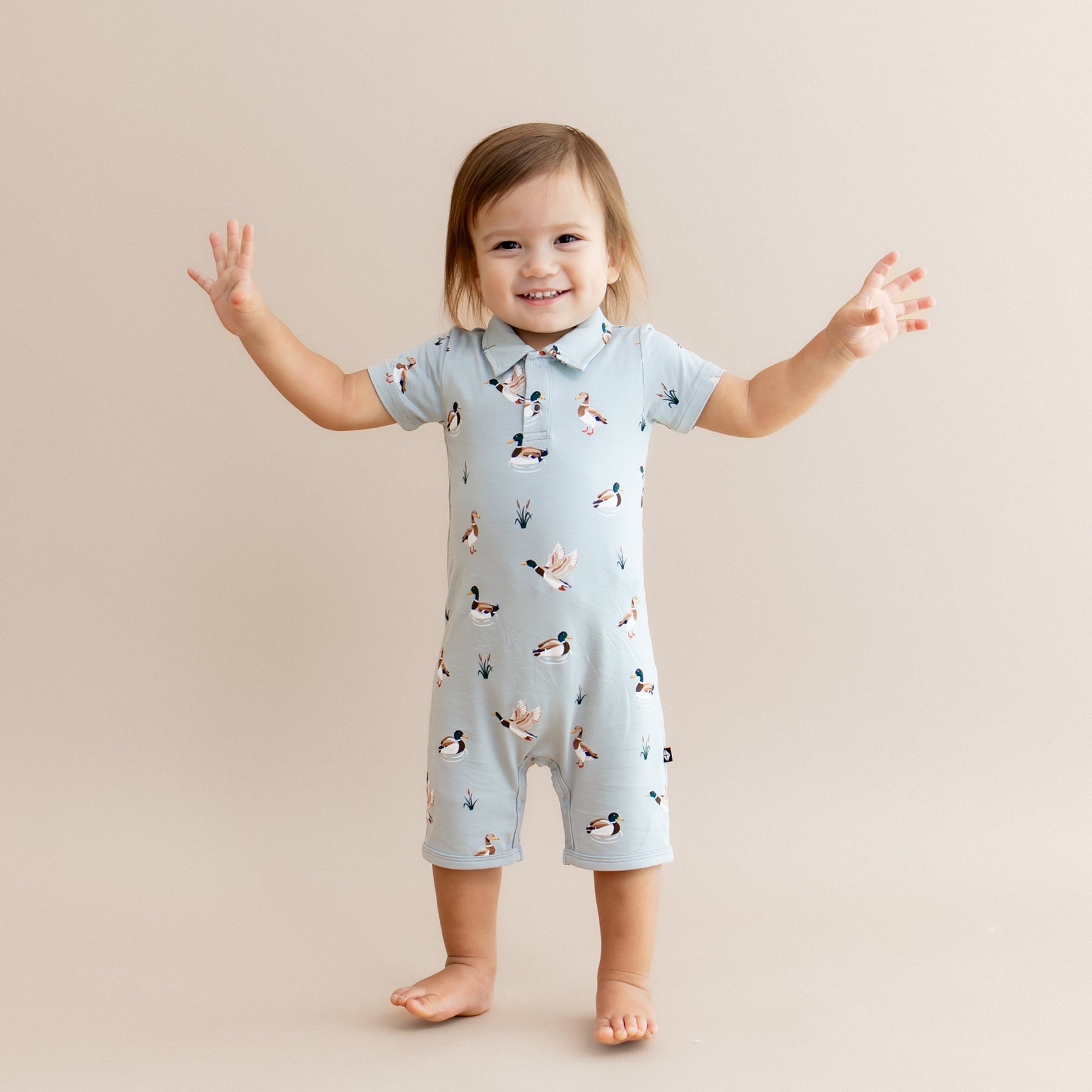 Young toddler standing with his arms out at the side wearing the Polo Shortall in Mallard Duck