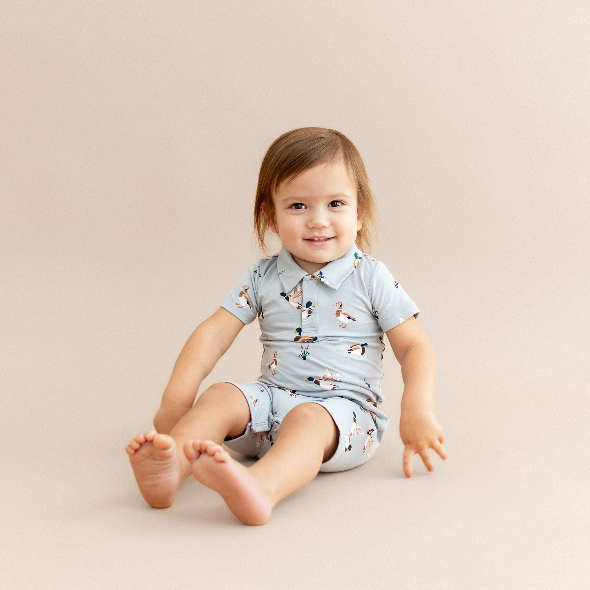 Young toddler sitting on the floor wearing the Polo Shortall in Mallard Duck