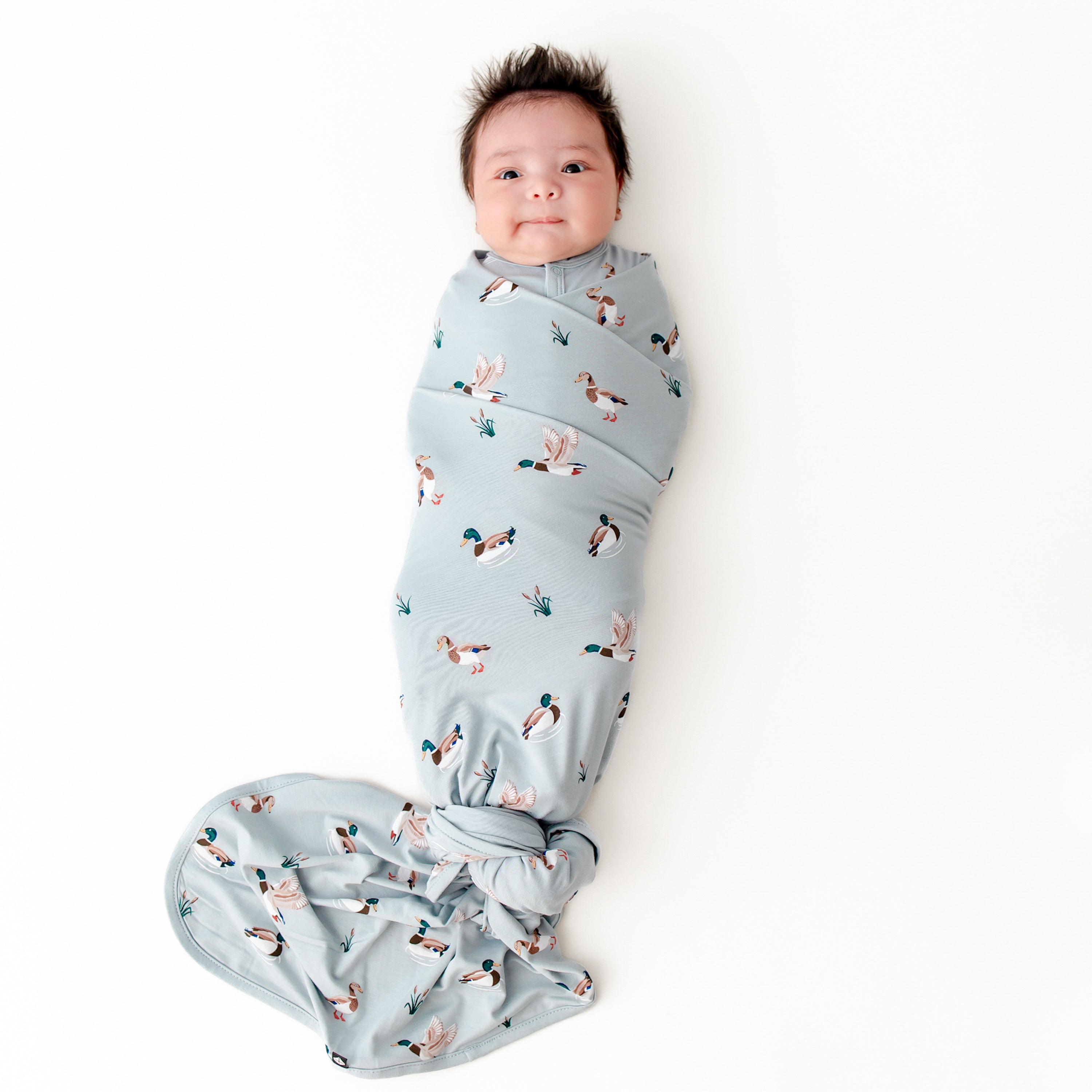 Newborn swaddled in the Swaddle Blanket in Mallard Duck laying on a white surface