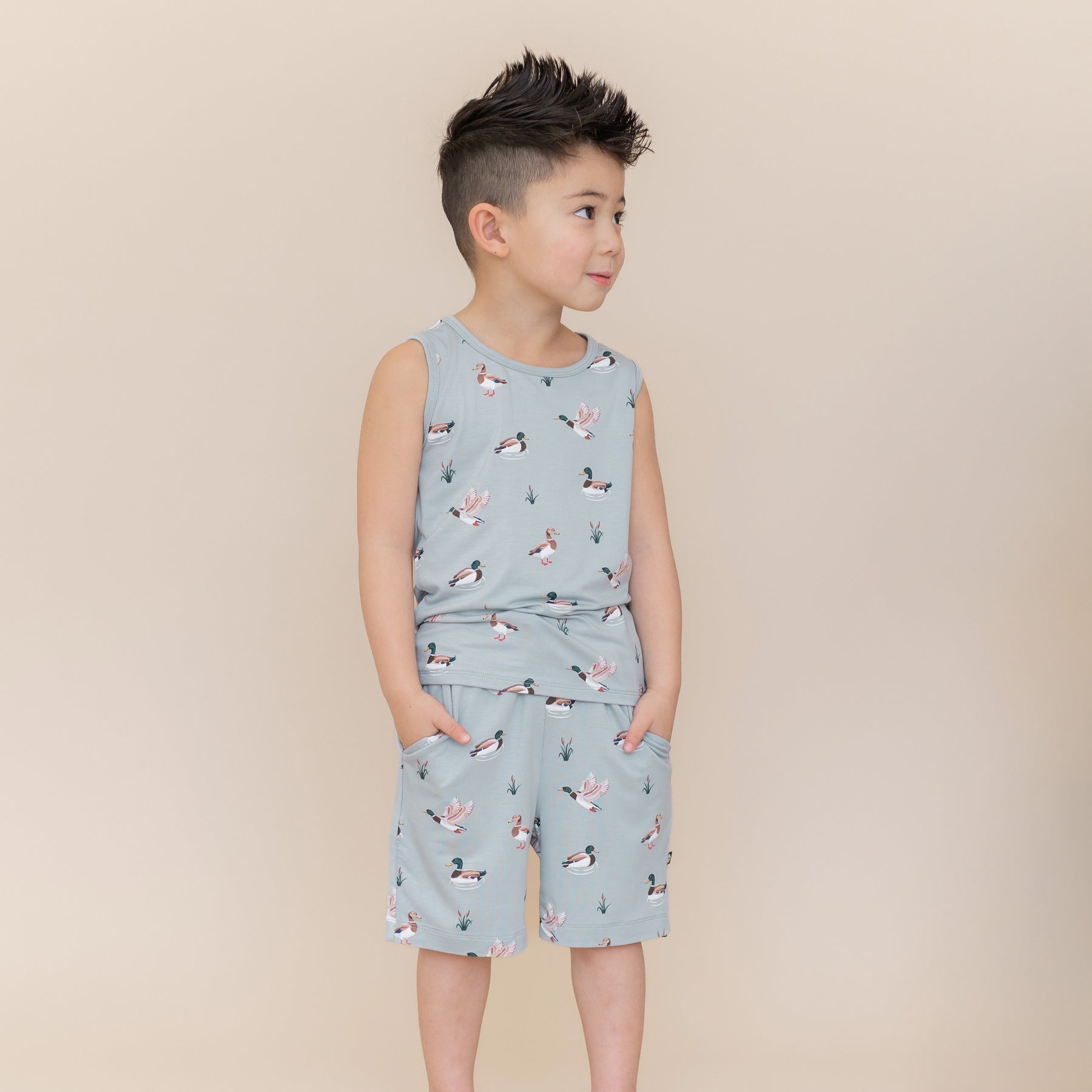Young boy posing wearing the Drawstring Short in Mallard Duck with both hands in his pockets paired with a matching toddler tank top