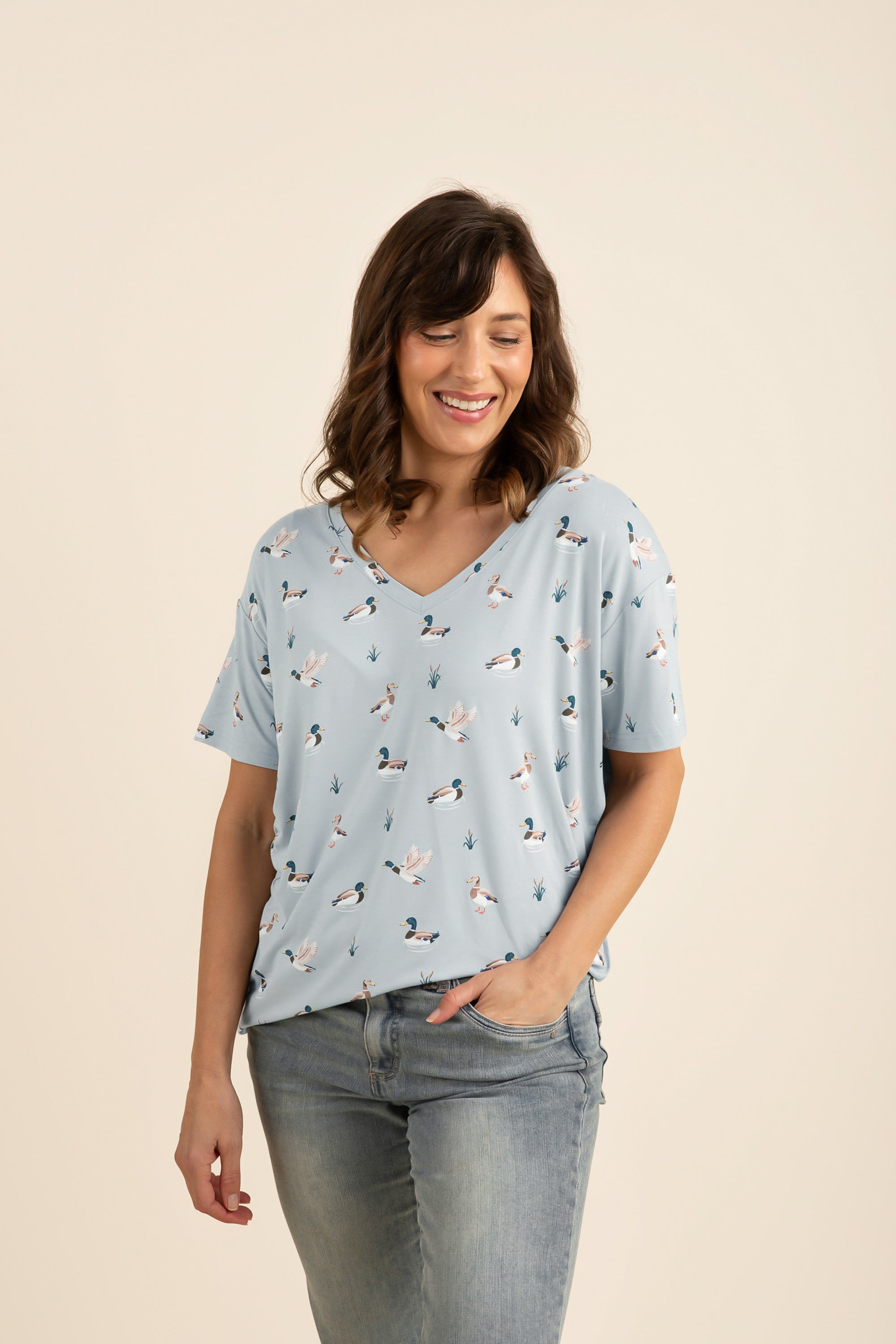 Woman wearing a light blue duck printed v-neck and jeans on a beige background