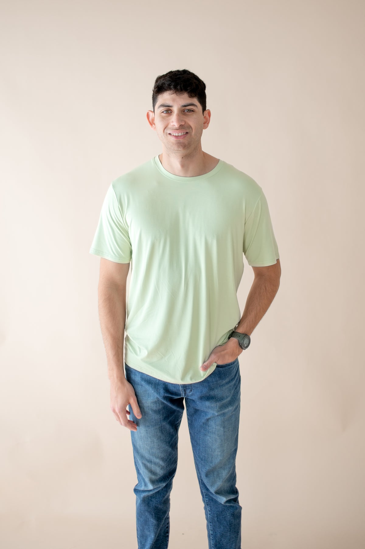 Male model wearing the Men's Crew Neck Tee in Basil paired the medium jeans in front of a neutral light background