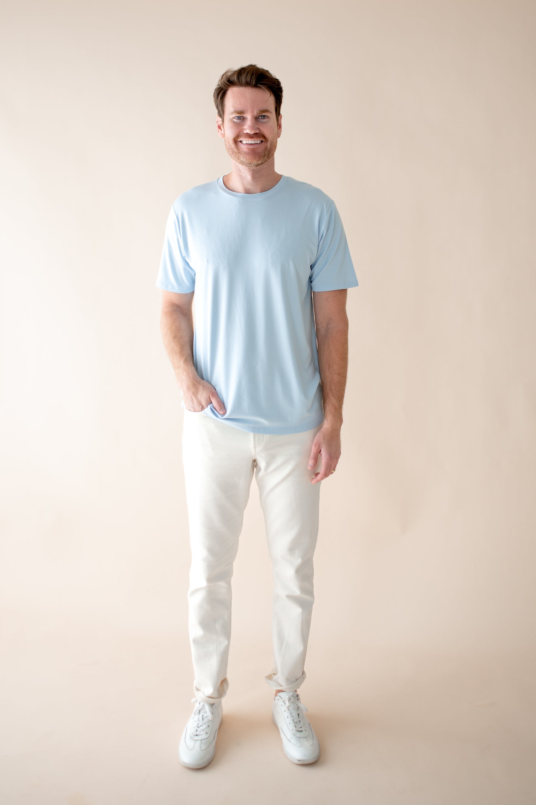 Smiling male model wearing the soft and breathable Men's Crew Neck Tee in Breeze paired with white pants with hand in pant pocket