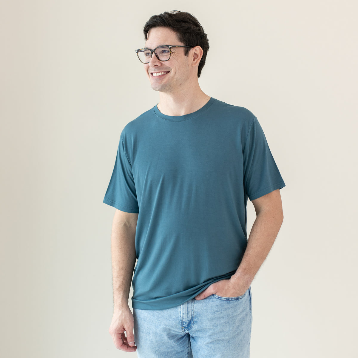 Smiling male model looking off to the side wearing the Men's Crew Neck Tee in Atlantic with one hand in his jeans pocket