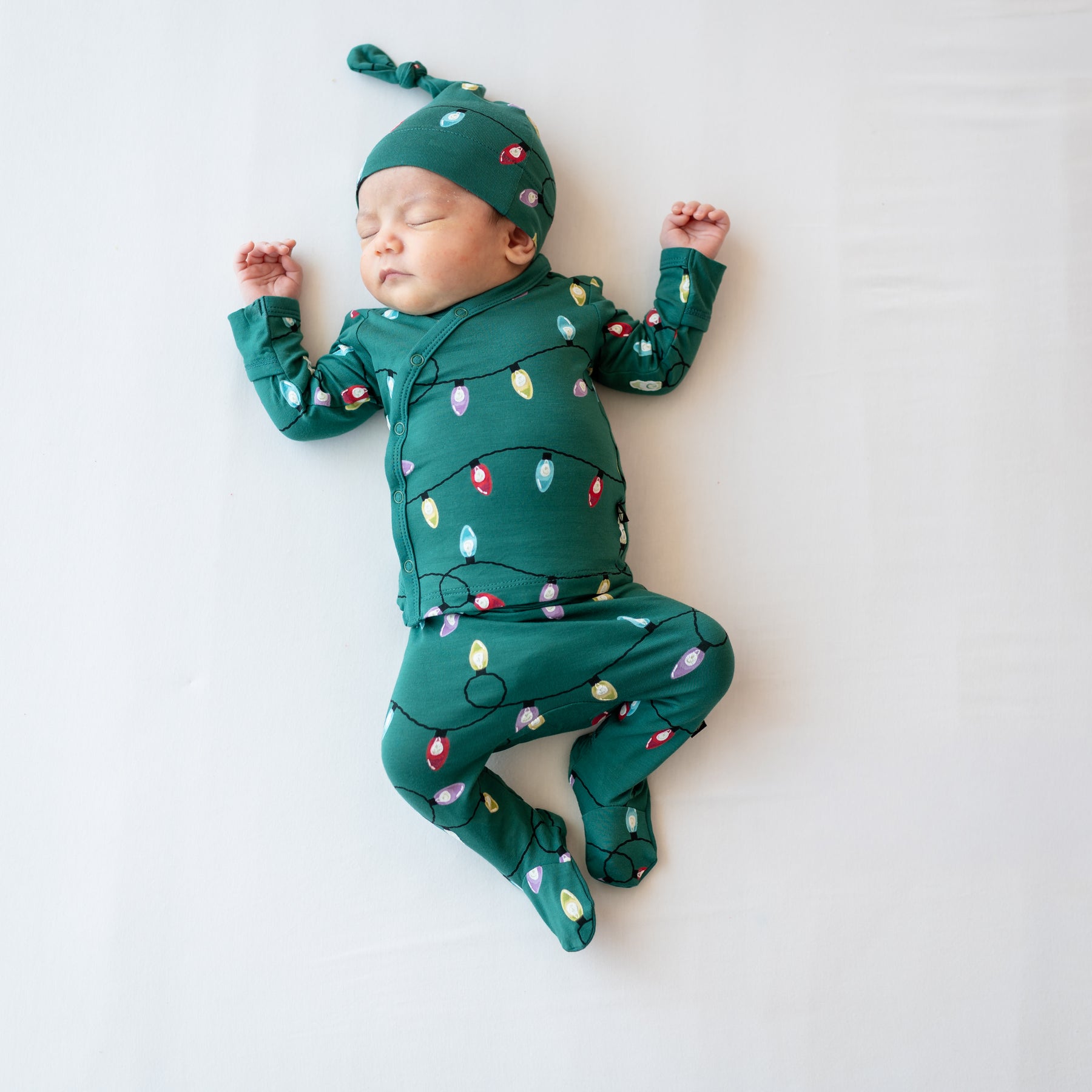 Sleeping Newborn laying on a light neutral background wearing the Take Me Home Set with Cap in Merry and Bright
