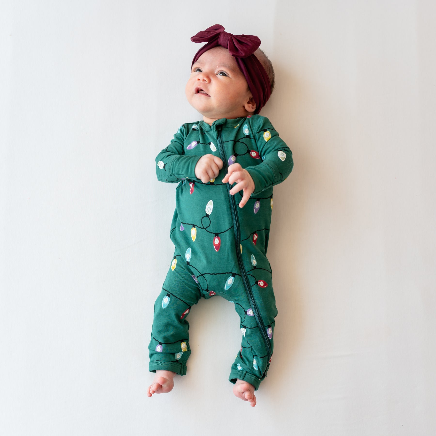 Newborn girl laying on a light neutral background wearing the Zippered Romper in Merry and Bright