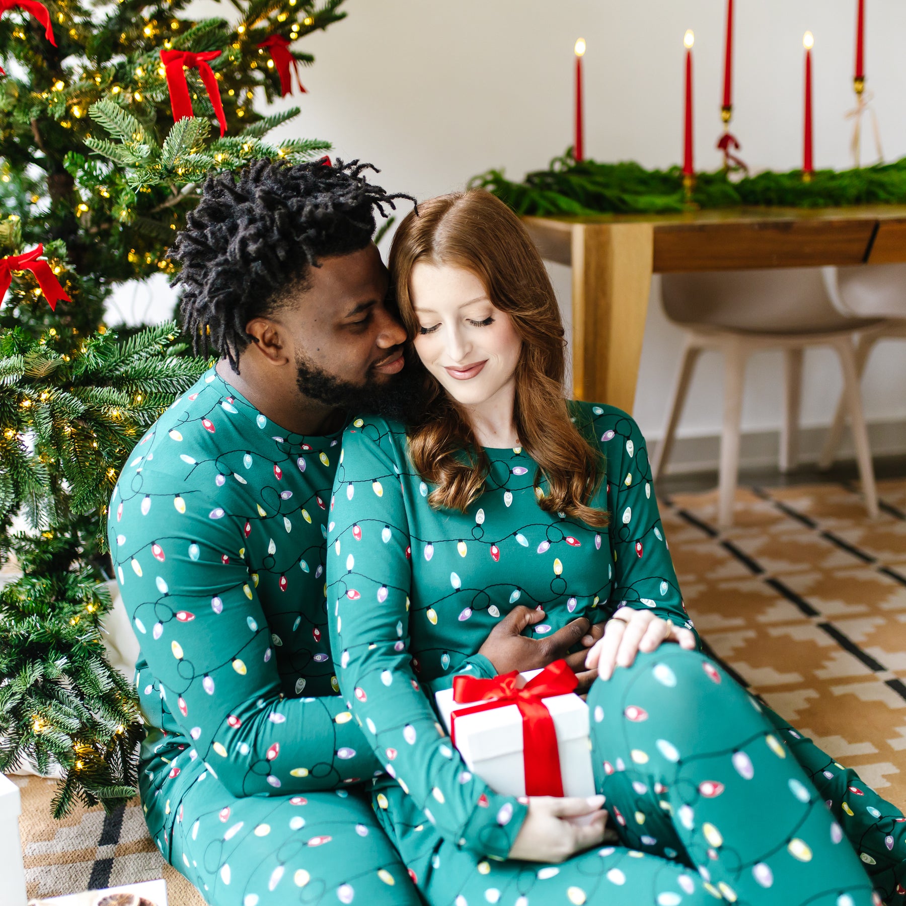 Couple sitting on the floor matching in the Women's and Men'sJogger Pajama Set in Merry and Bright