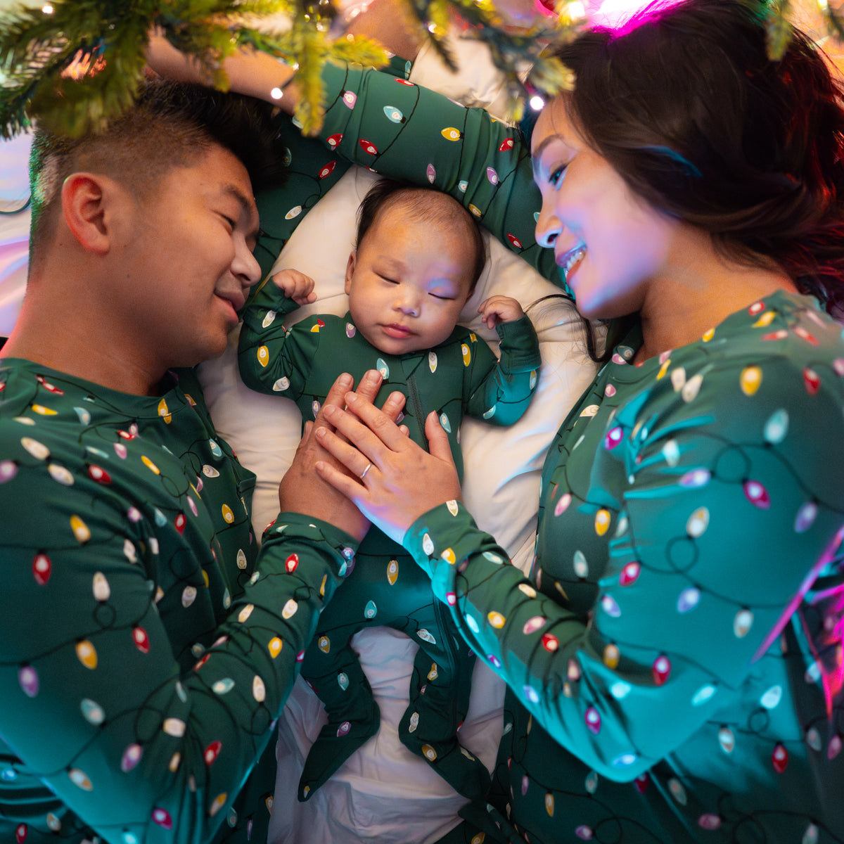 Family of three laying under a decorated Christmas tree all matching in the Merry and Bright Holiday print