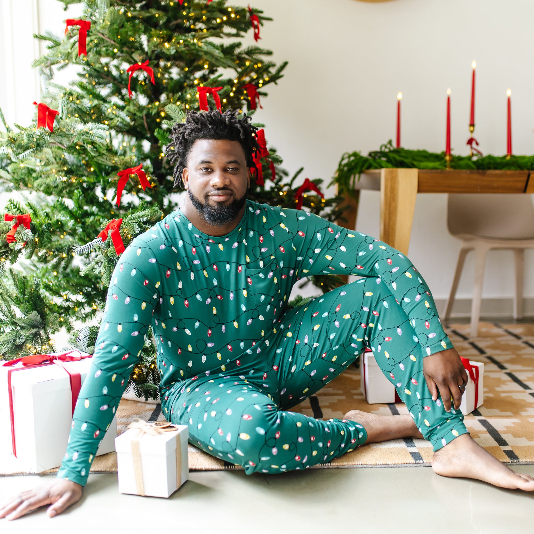Male model sitting on the floor in front of a decorated Christmas tree wearing the Men's Jogger Set in Merry and Bright
