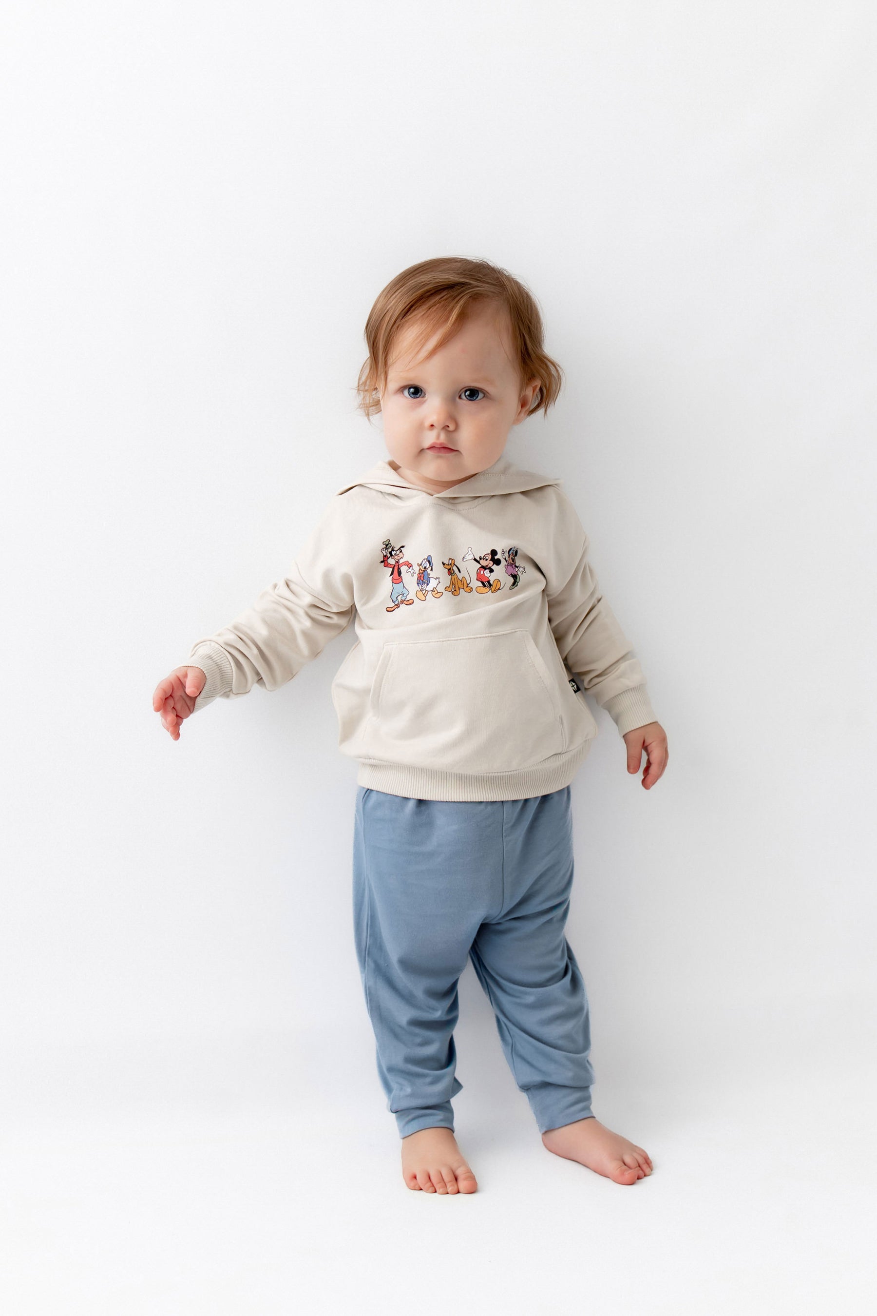 Toddler standing wearing mickey mouse  friends hoodie with blue pants.