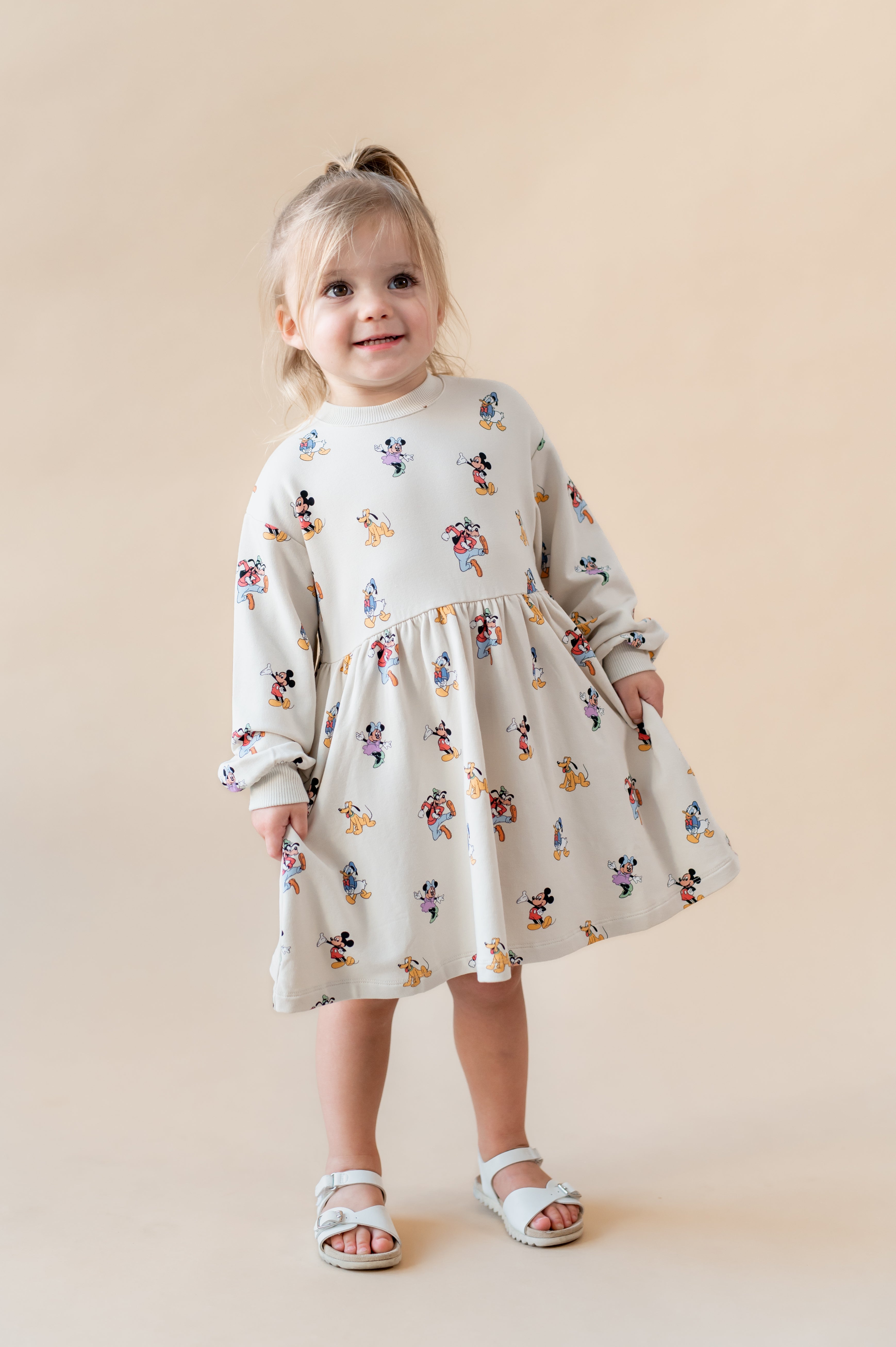 Toddler girl smiling wearing a long sleeve skater dress in mickey mouse & friends.