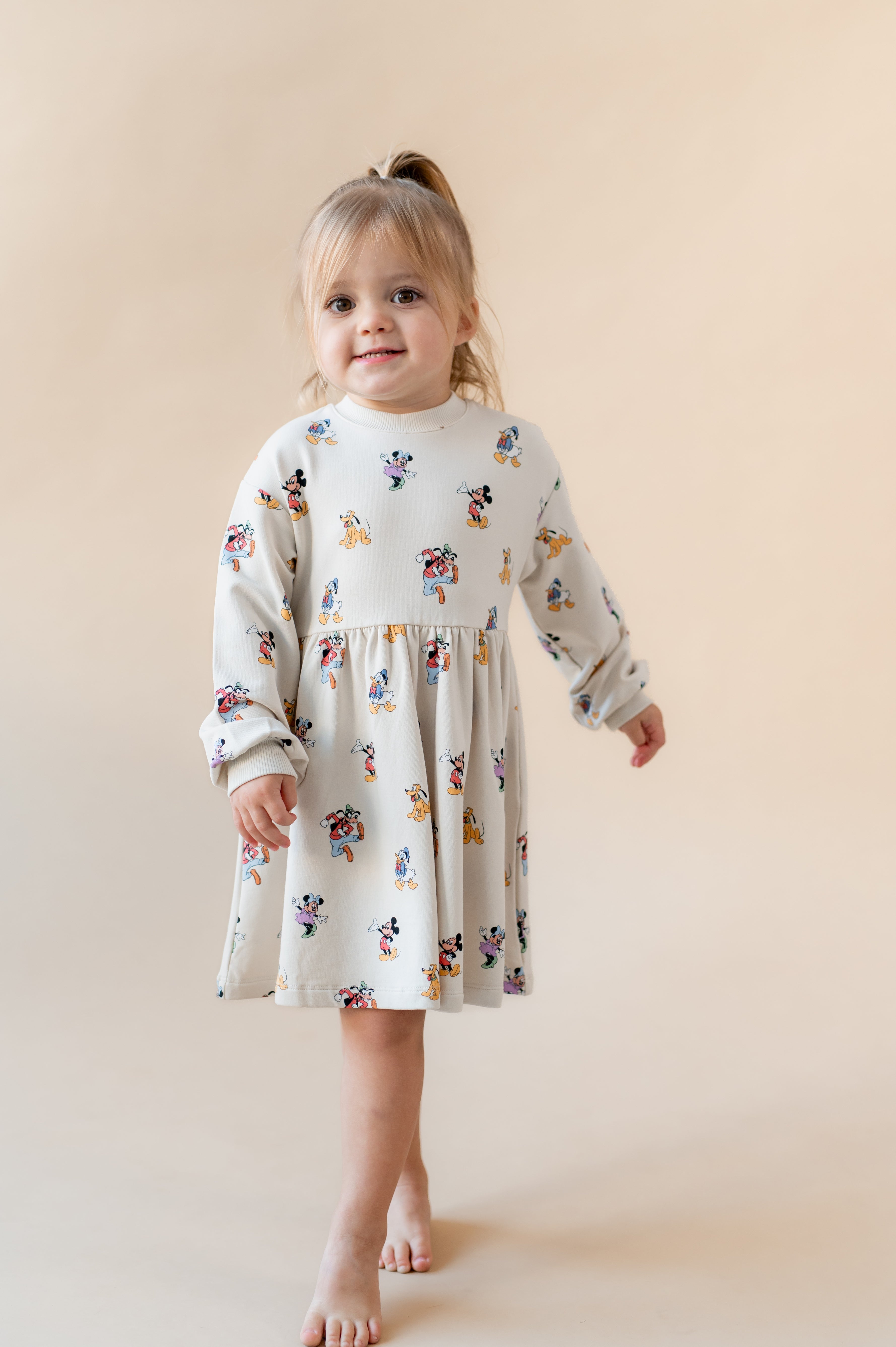 Girl standing on her toes smiling wearing mickey mouse & friends dress.