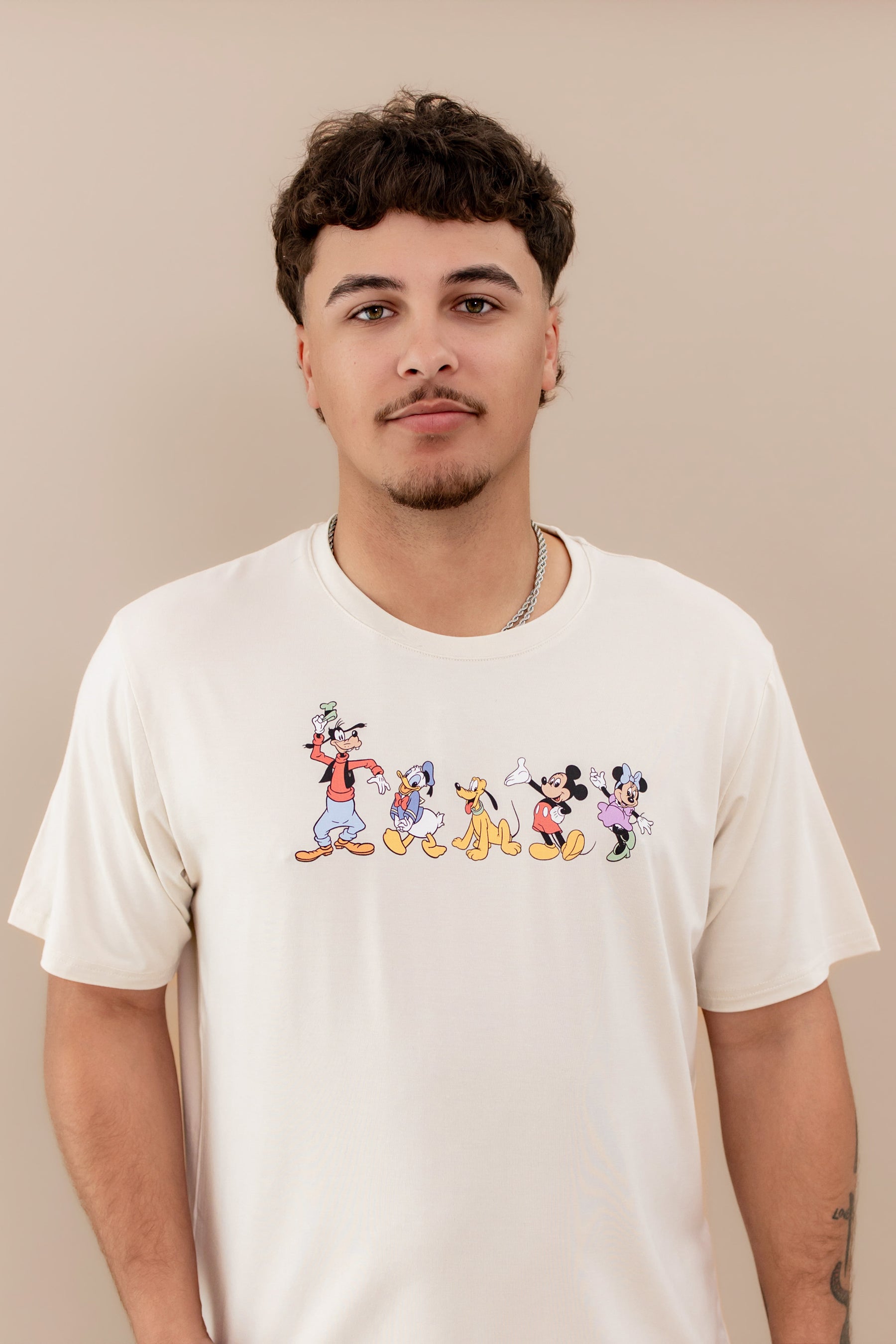 Man wearing a cream colored tshirt with mickey characters on the chest