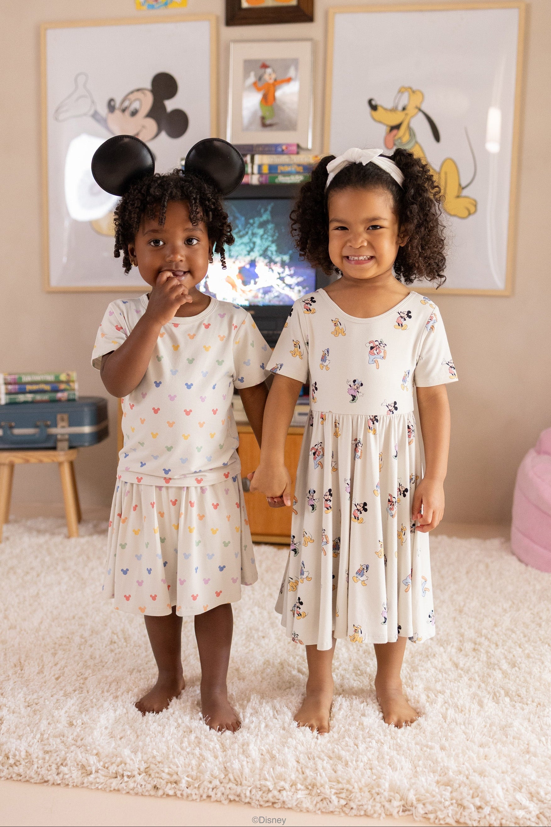 two girls wearing Disney x Kyte collection featuring mickey patterns in a nostalgic room with mickey posters and vintage TV