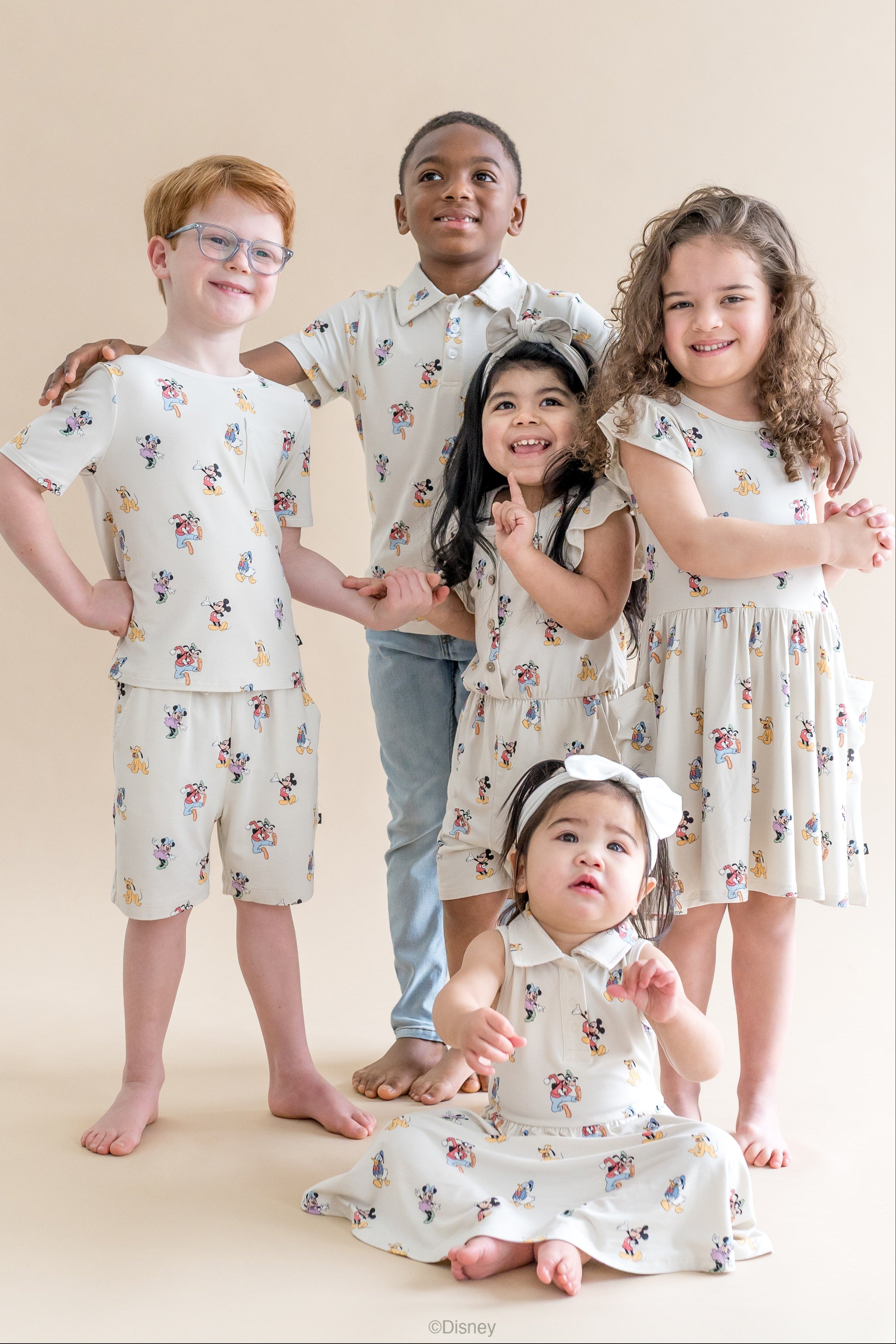 Five children wearing matching outfits with a mickey and friends pattern on a beige background
