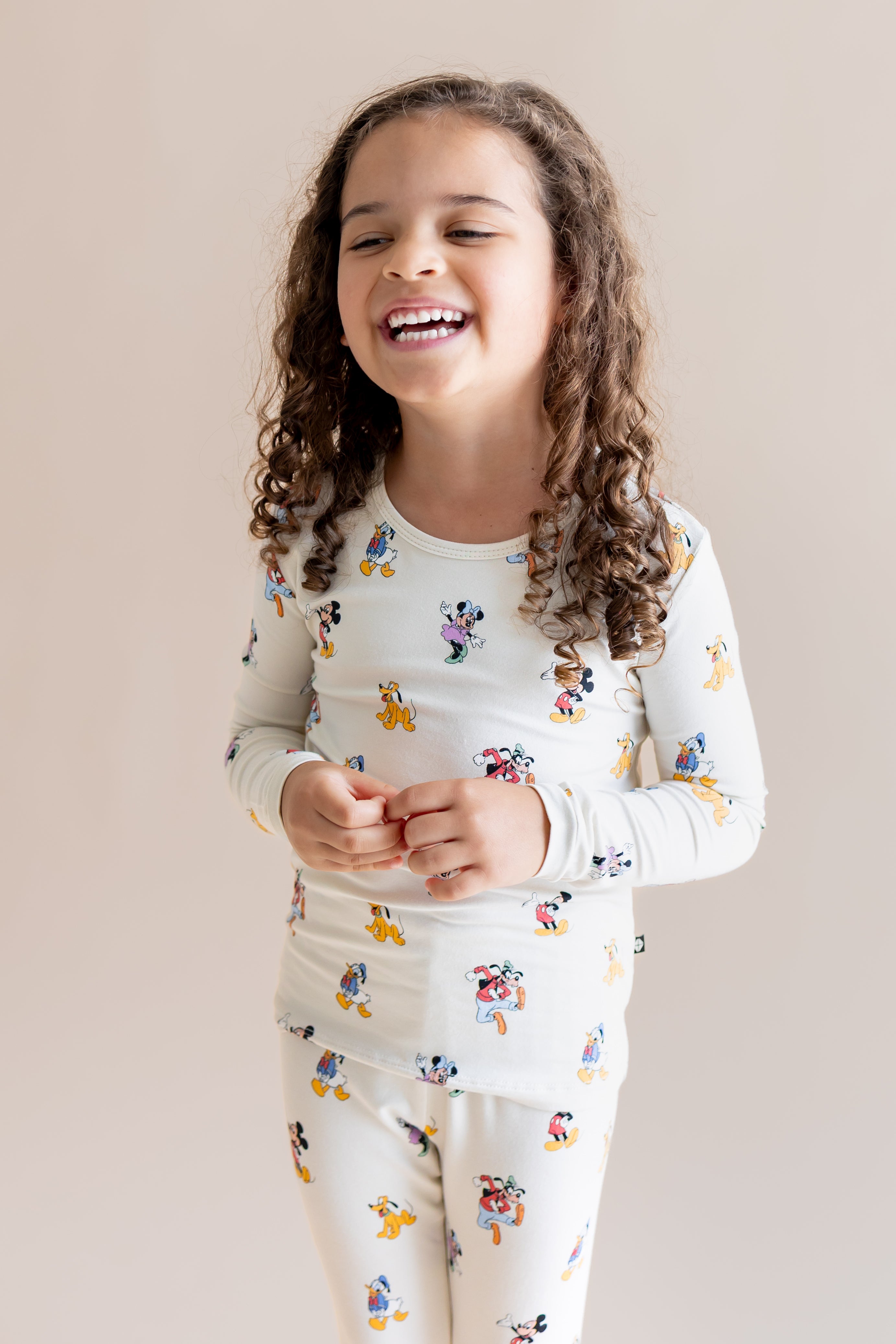 Girl smiling in Long Sleeve Pajamas in Mickey Mouse & Friends print on a cream background