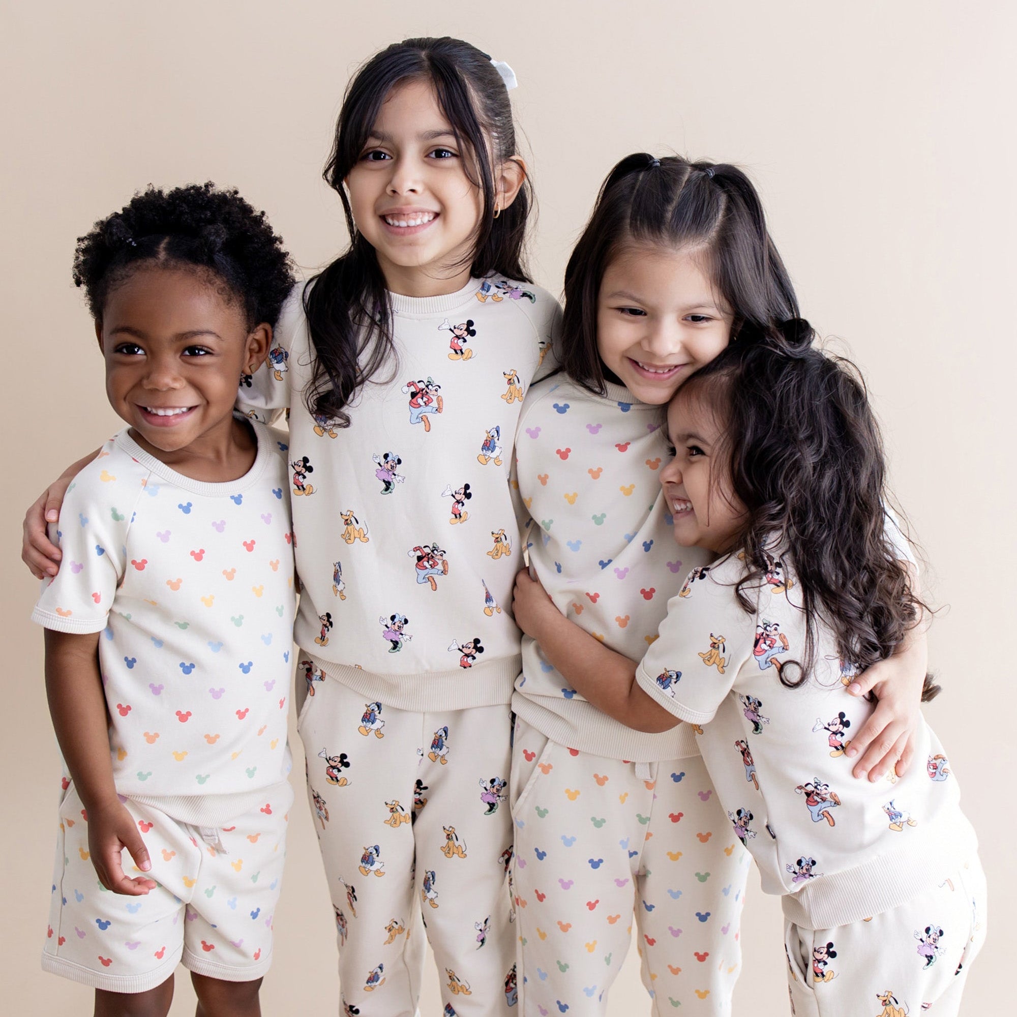 Four children wearing matching mickey and friends sets with a neutral background
