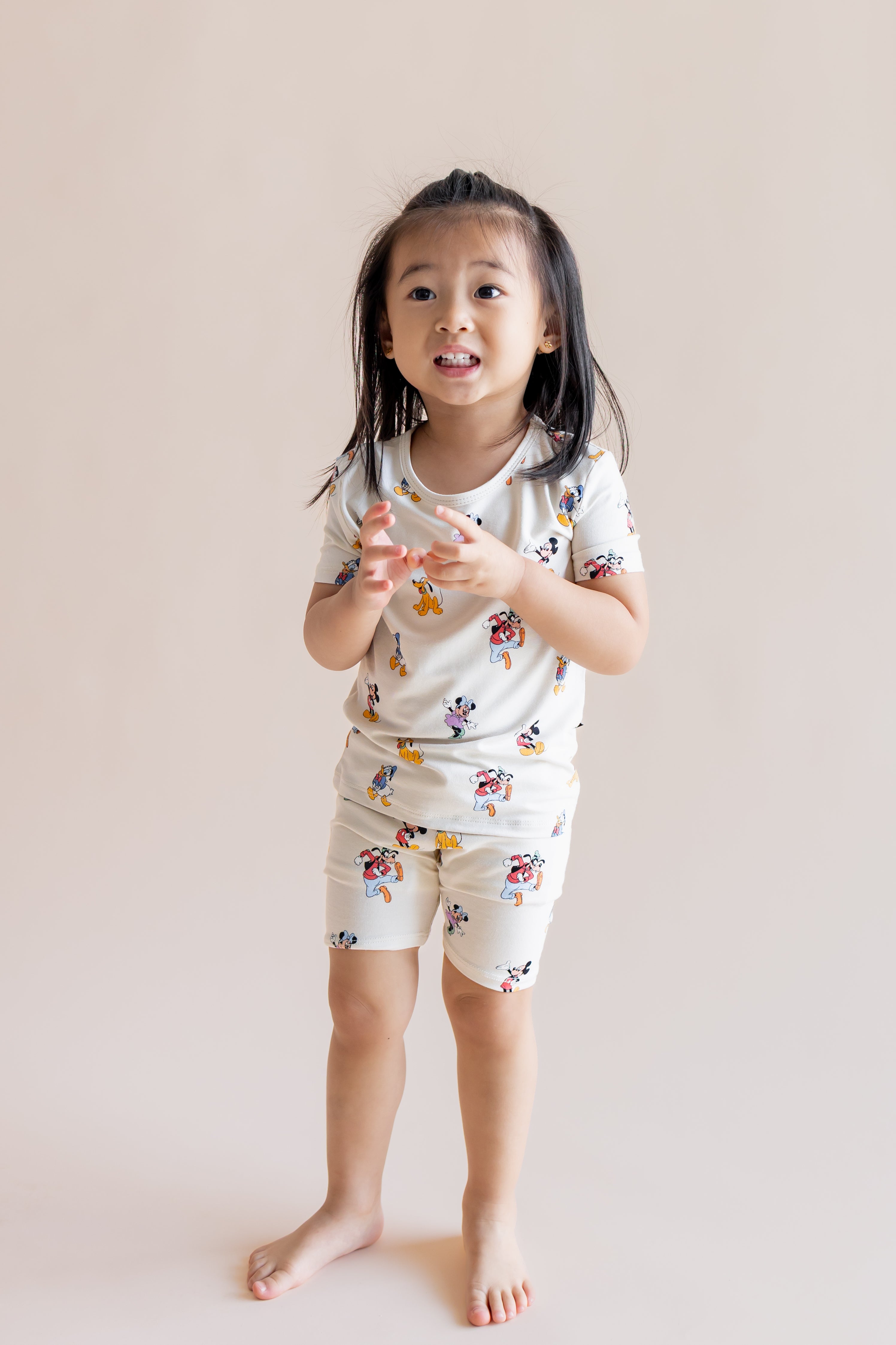 Girl wearing Short Sleeve Pajamas in Mickey Mouse & Friends print standing on a cream background
