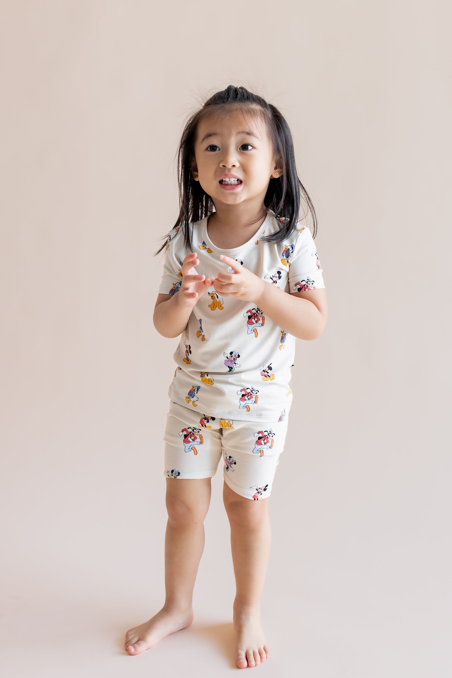 Girl wearing Short Sleeve Pajamas in Mickey Mouse & Friends print standing on a cream background