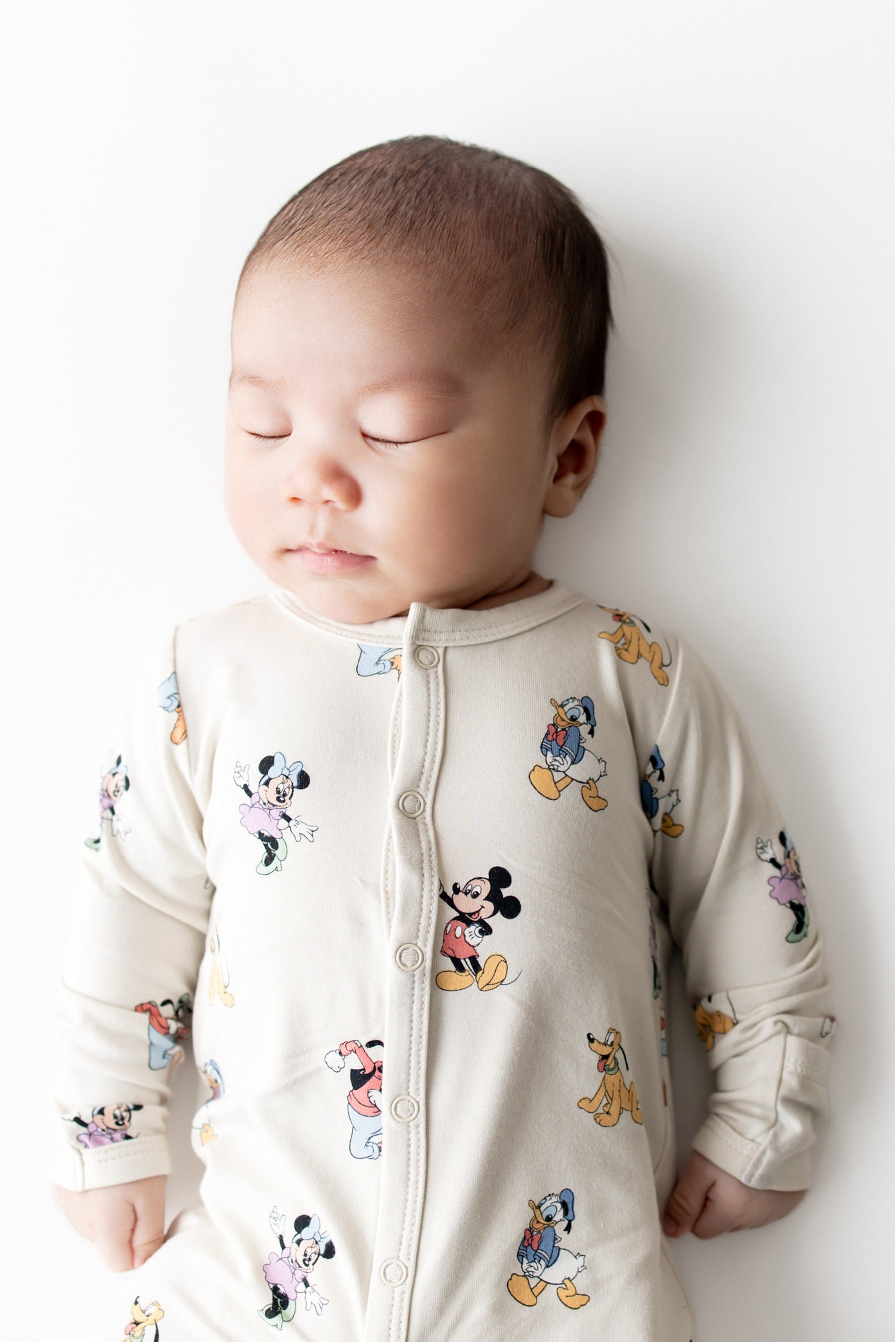 Baby wearing a snap romper with cartoon character prints against a white background